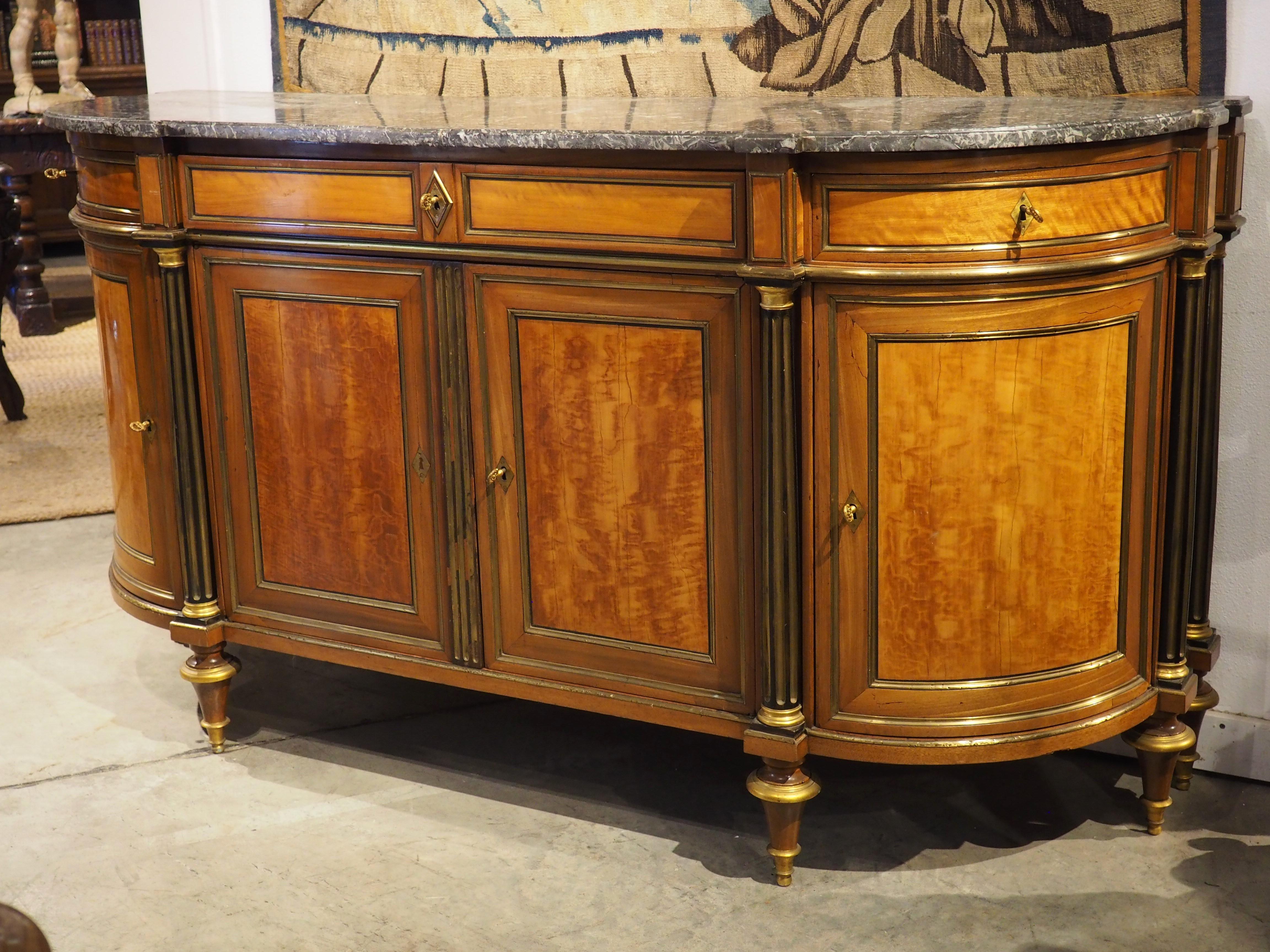 A grand demi-lune buffet from the period of Louis XVI, this French sideboard was hand-carved circa 1780, using a combination of mahogany and lemonwood. Topped by a one-inch thick gray Saint Anne marble, the buffet has a wonderful, warm palette. The
