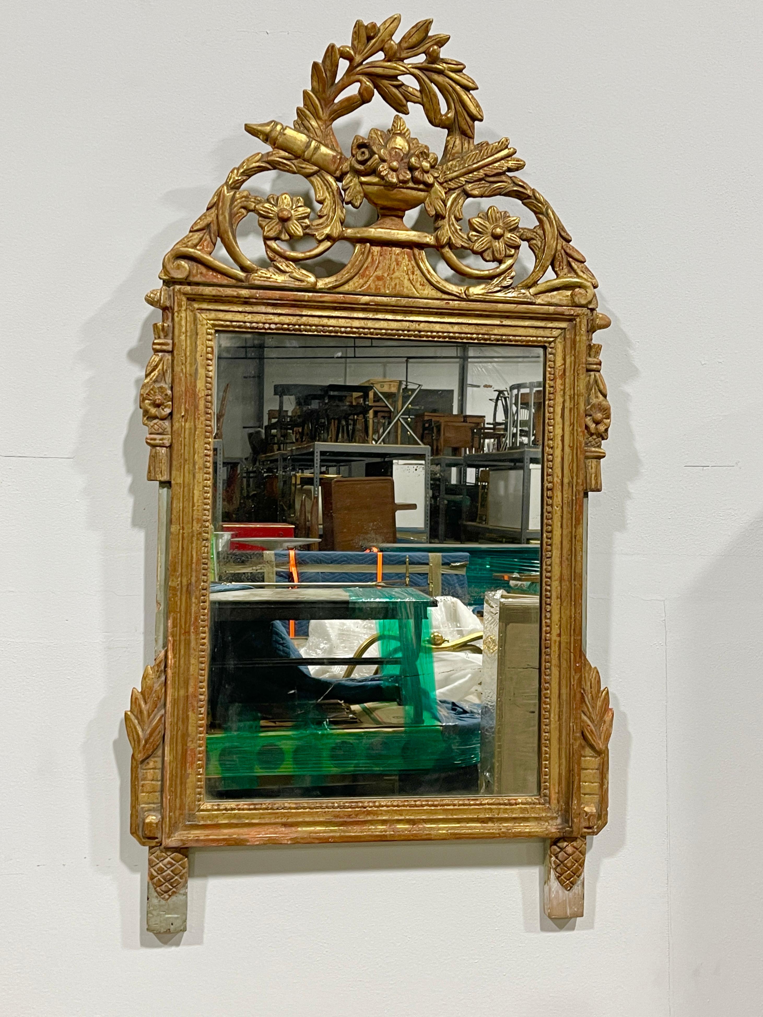 Miroir français Louis XVI en bois doré avec de jolis détails sculptés, surmonté d'une couronne finement sculptée avec une forme d'urne centrale, un carquois et une flèche, des feuilles d'acanthe et des formes végétales. Peut-être un blason de