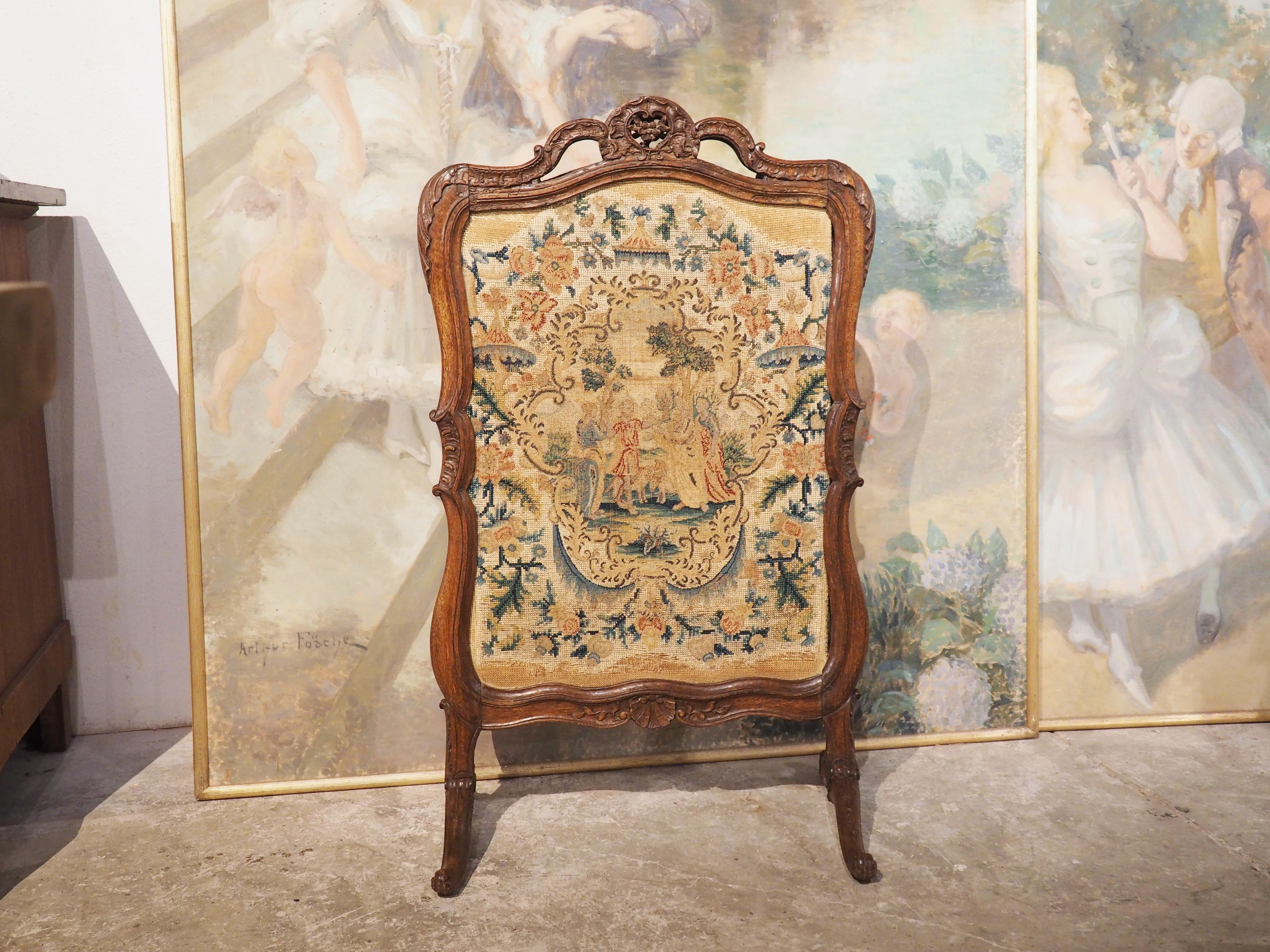 Used during warm months to cover the opening of a fireplace, this French period Regence firescreen with needlepoint inset is from circa 1720. The hand-carved wood frame has motifs in the Regence style, such as the scalloped shell on the bottom that