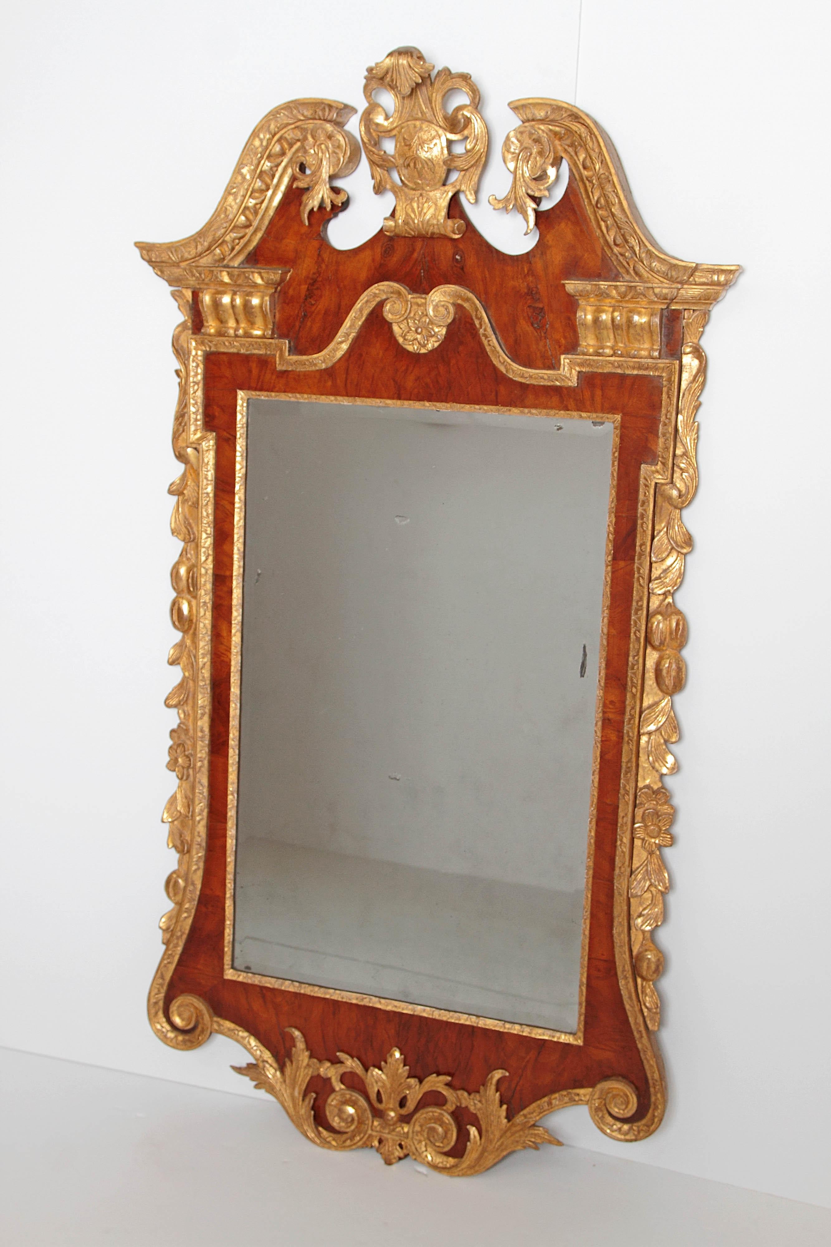 A circa 1740, period George II pier glass / mirror with beautiful bookmatched walnut veneers and having carved gilded embellishments, broken pediment top with gilded center shield surrounded by acanthus leaves and gilded floral cascades down each