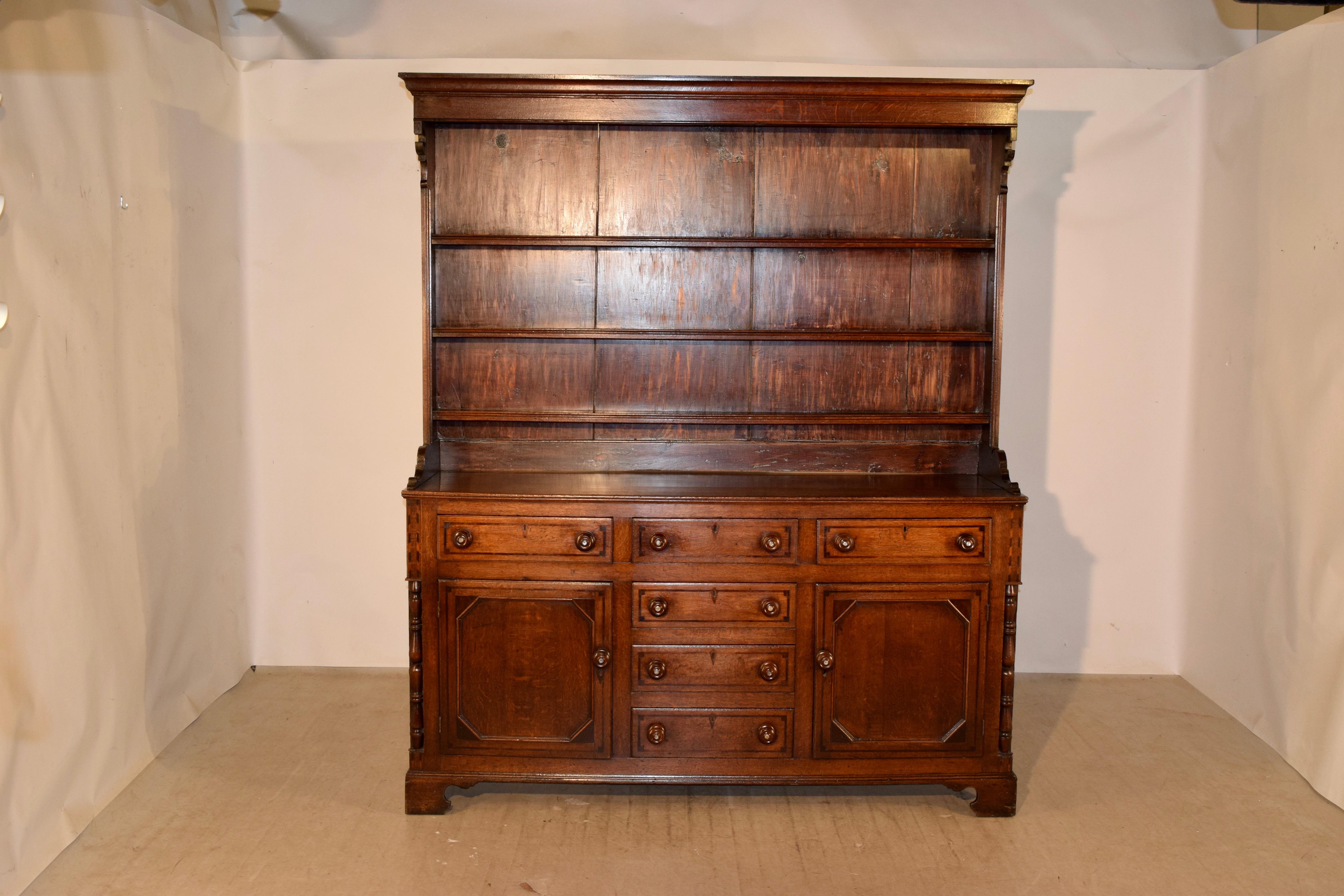 Period Georgian Welsh dresser made from oak and pine, circa 1780-1820. The cupboard has a stately crown molding over three shelves, with decorative shaped corbels on the sides of the shelf, following down to a base with raised paneled sides and