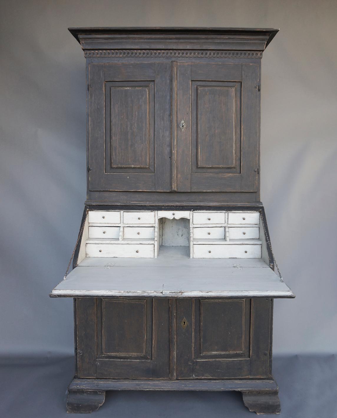 Black Gustavian secretary in two parts, Sweden, circa 1810. The upper section has a guilloche frieze under the flared cornice and two raised panel doors with shelved behind. The lower section has a fitted interior behind the slant-front. The