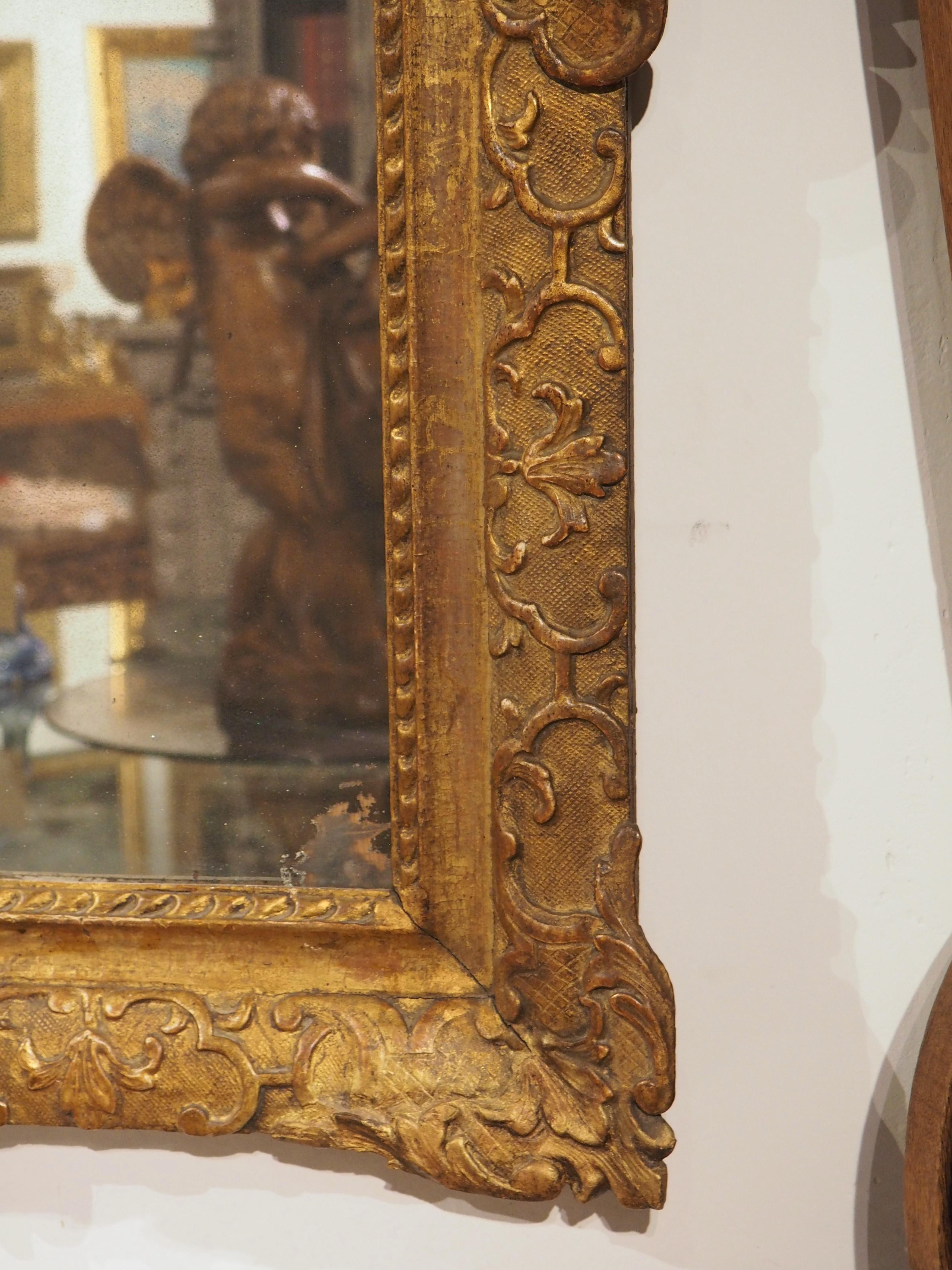 Ce miroir d'époque Louis XIV présente des motifs sculptés parmi les plus élégants. Il s'agit de motifs tels que le lambrequin, la feuille d'acanthe, les attributs martiaux, les palmettes, les fonds à motifs, le lys schématique ou la fleur de lys.