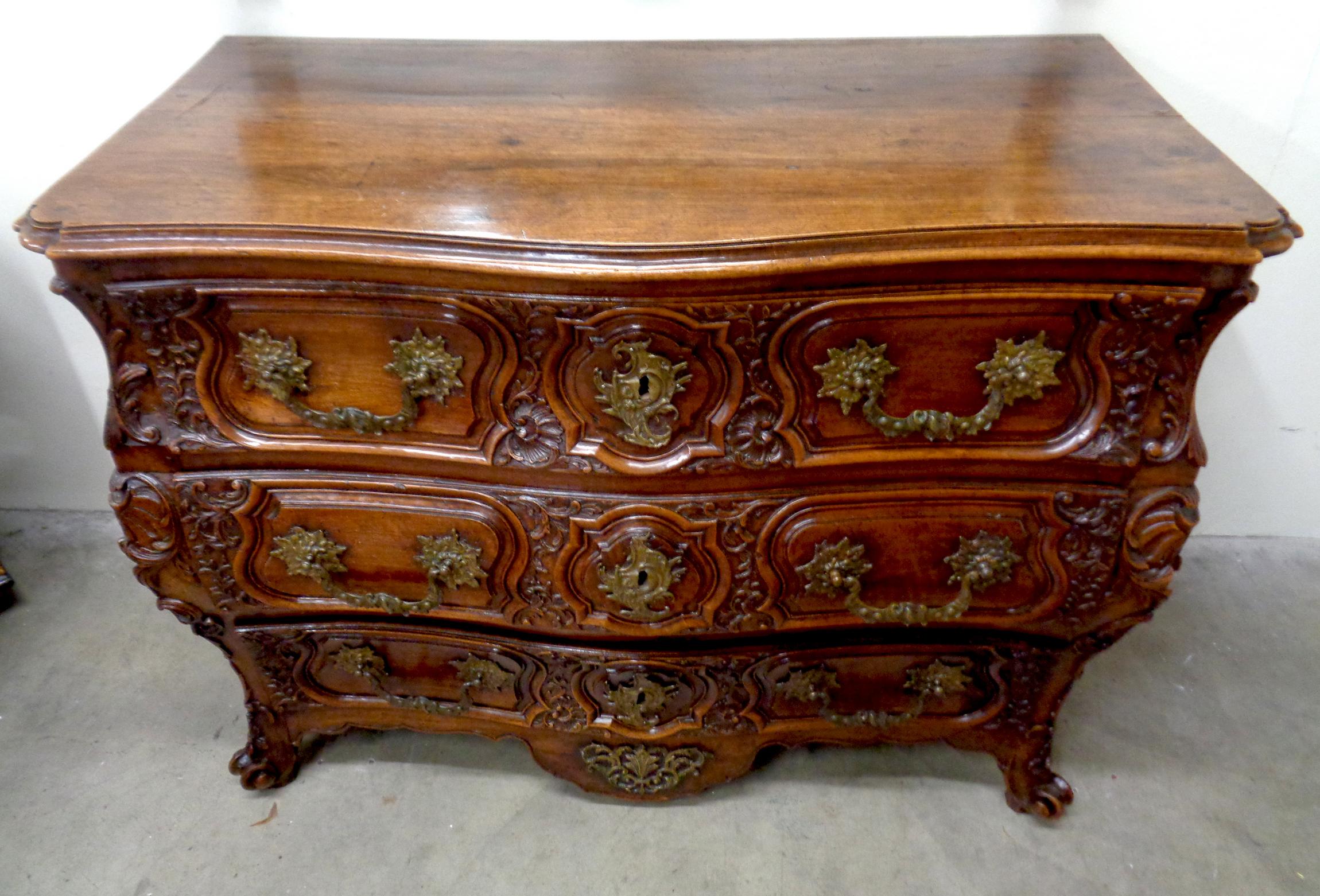 French walnut museum quality three-drawer Lyonnaise commode, circa 1730-1740. The commode is beautifully carved throughout and has richly colored patination. It has original chased bronze drawer pulls and key escutcheons. The face of the commode is