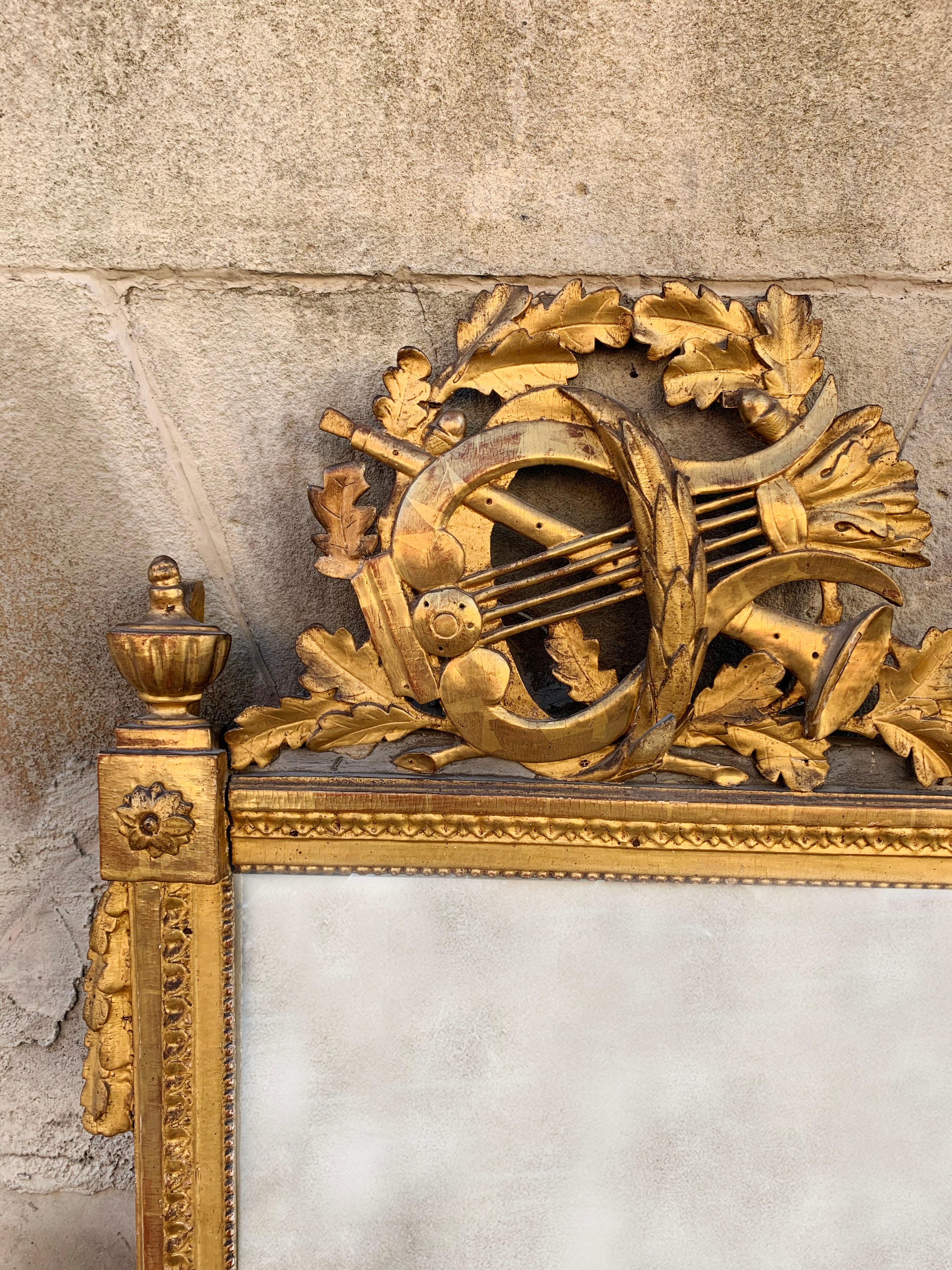 A beautiful gilded looking glass from late 18th century France with beautiful detailing and patina. The corona exhibits a laurel wreath and lyre harp, attributes of the god Apollo. The corners of the mirror frame are decorated with rosettes and the