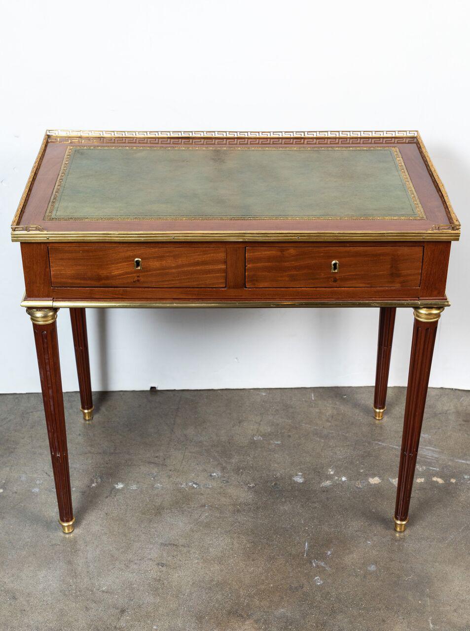Beautifully proportioned, two drawer, ladies, mahogany writing desk with embossed and parcel-gilt leather top surrounded by a pierced, Greek Key style, ormolu border. A pull-out, writing extension is nested beneath the drawers and features the same,