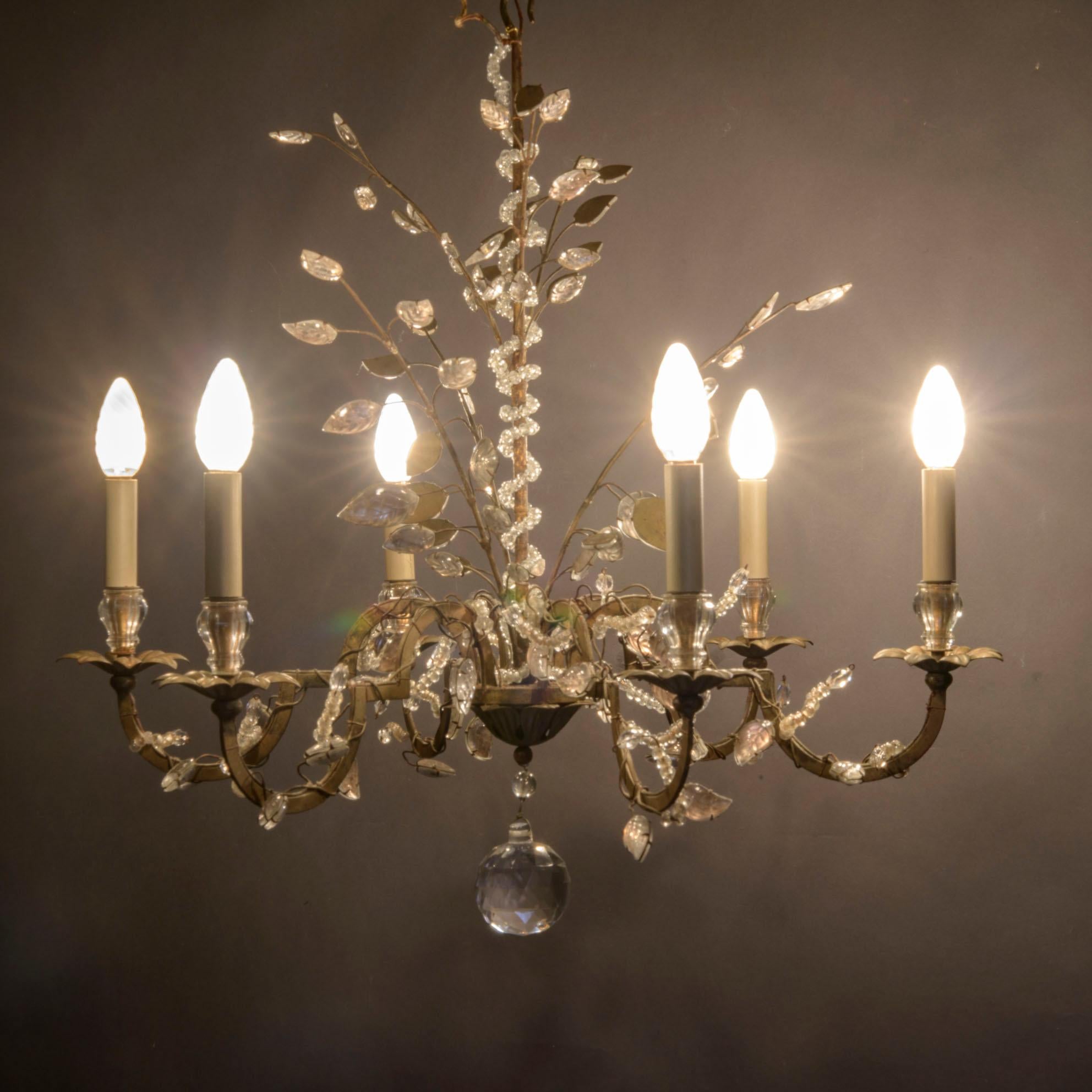 Wonderful six-arm original Baguès French gilt bronze transitional chandelier, decorated with glass shoots, as well as rock crystal small, delicates leaves. 
The shape is a round with a flowing crown. 
All the gilt iron is lined with decorative
