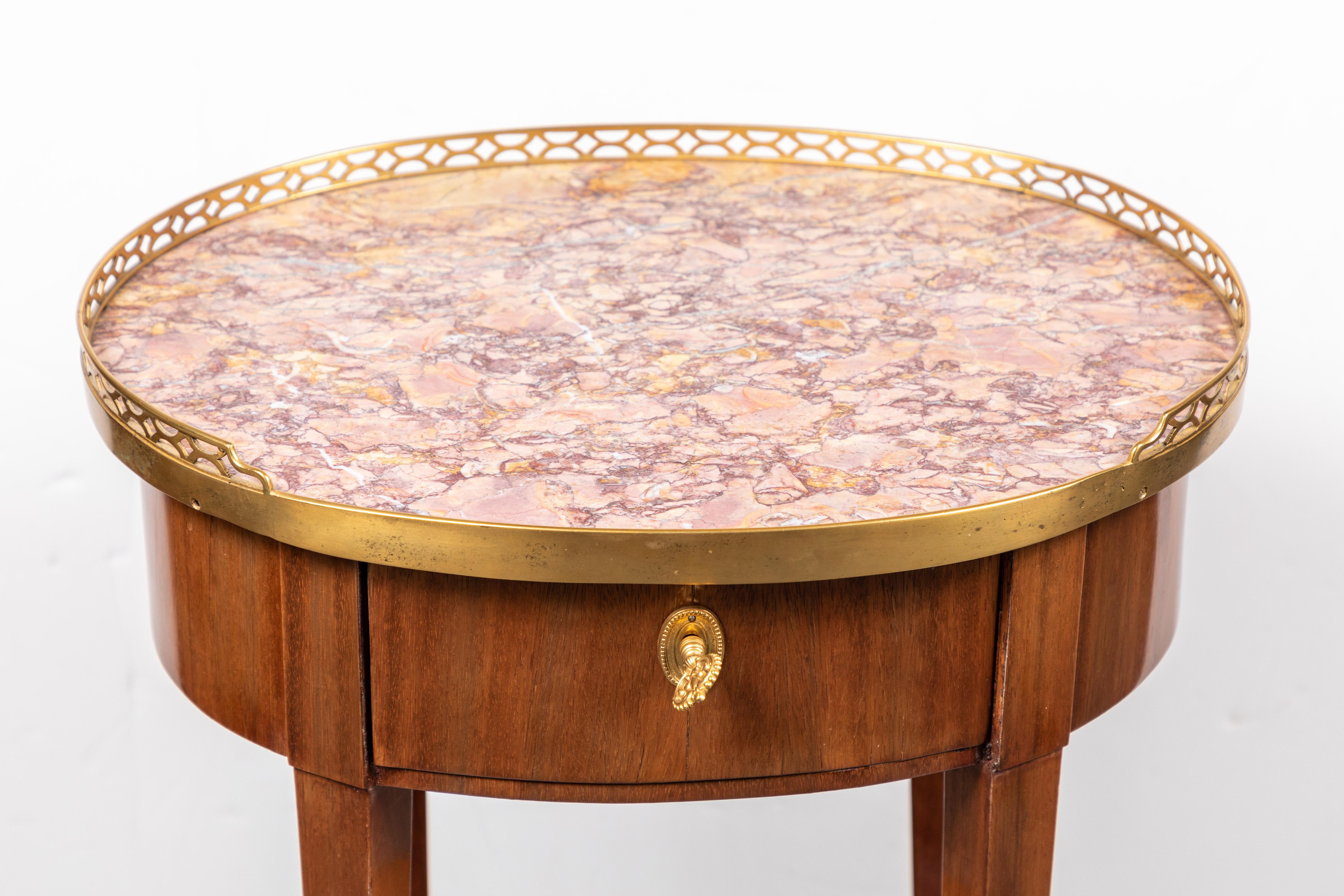 A fine, turn-of-the-century, French, single-drawer, veneered side table on tapered legs capped by ormolu feet. The oval top inset with rouge marble and surrounded by a pierced bronze parlour.