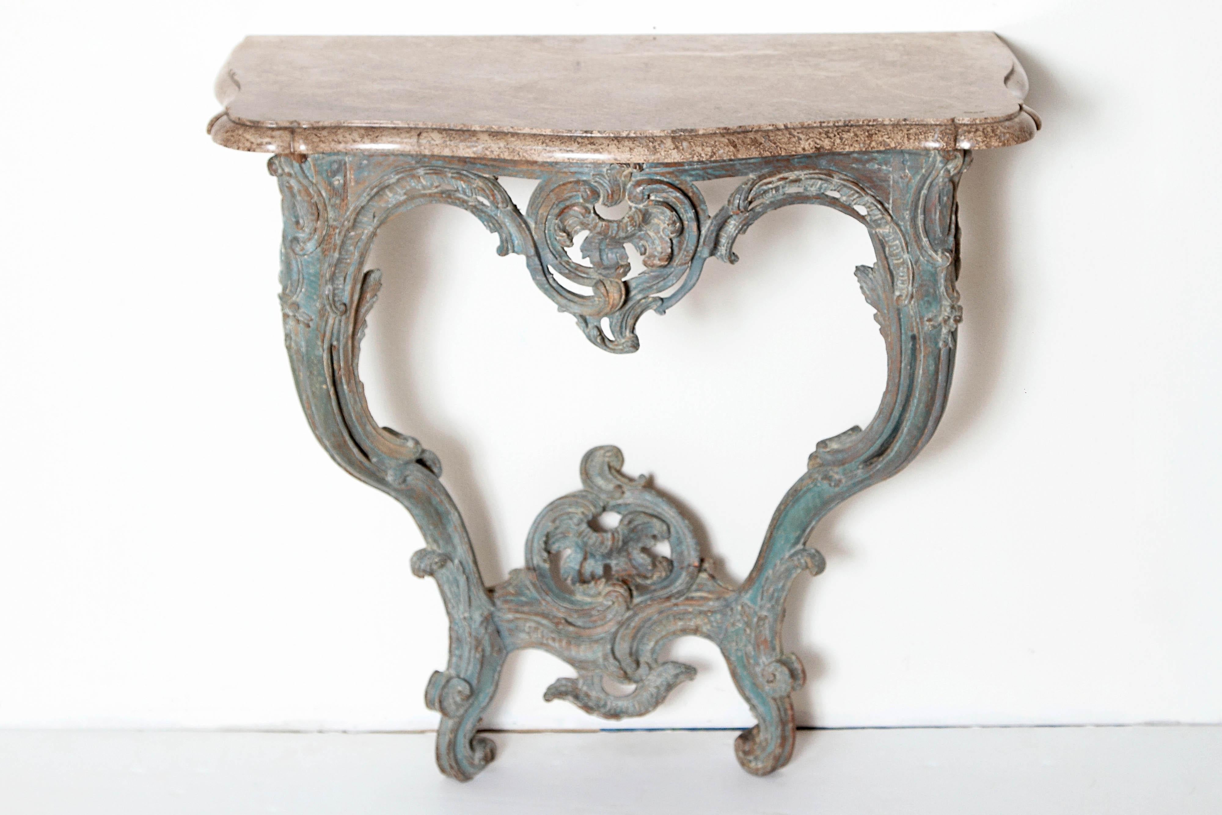A French Louis XV highly carved / Rococo console with original blue paint. Surmounted by a serpentine moulded beige marble top above a rocaille cartouche. The frieze is scroll-carved and pierced. Two cabriole legs connected with a rocaille