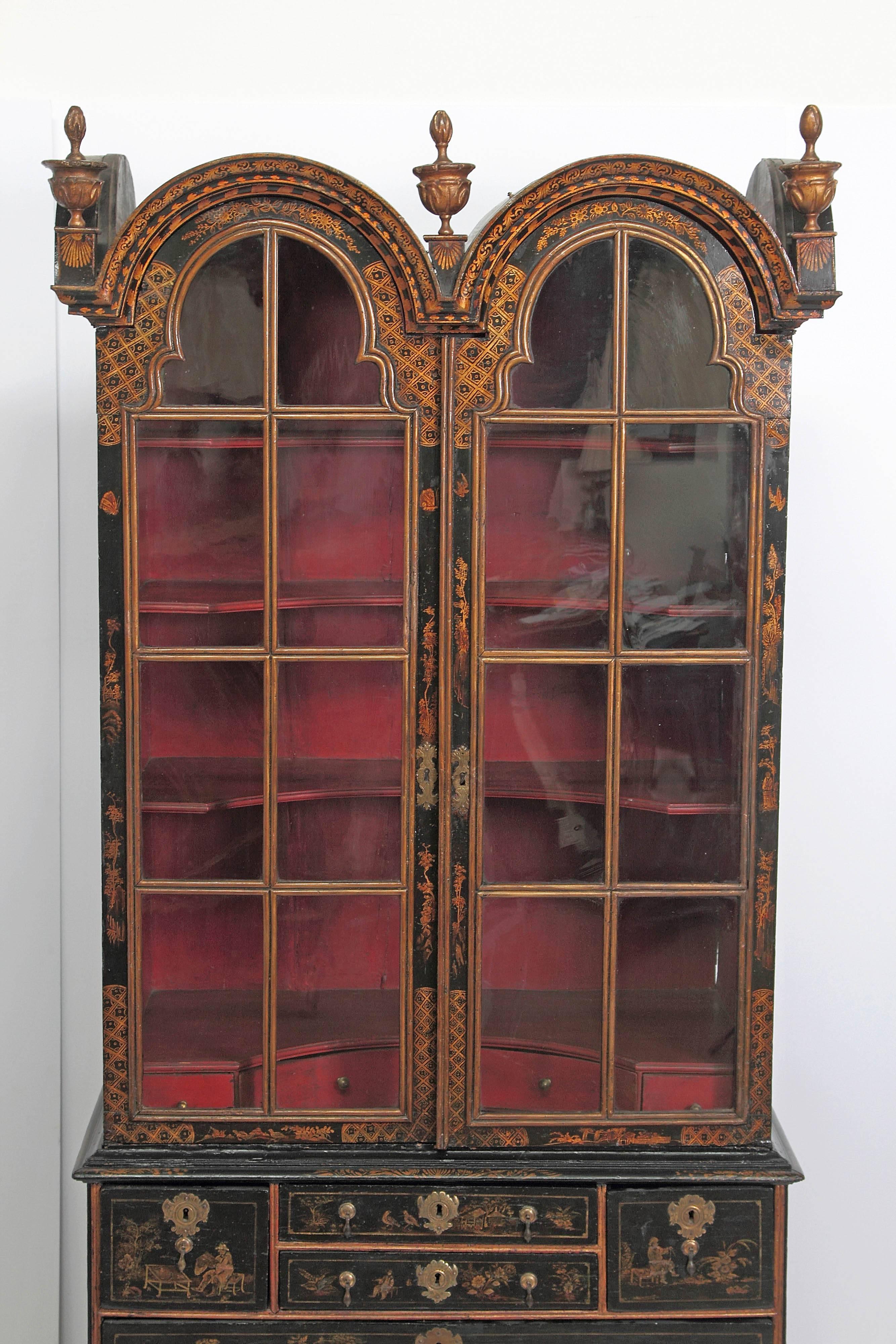A period Queen Anne cabinet with glass paned doors over a chest of drawers, the whole rests on bun feet, double-bonnet top with three flaming urn finials, the upper cabinet interior is red and fitted with shaped / concave shelves and a series of
