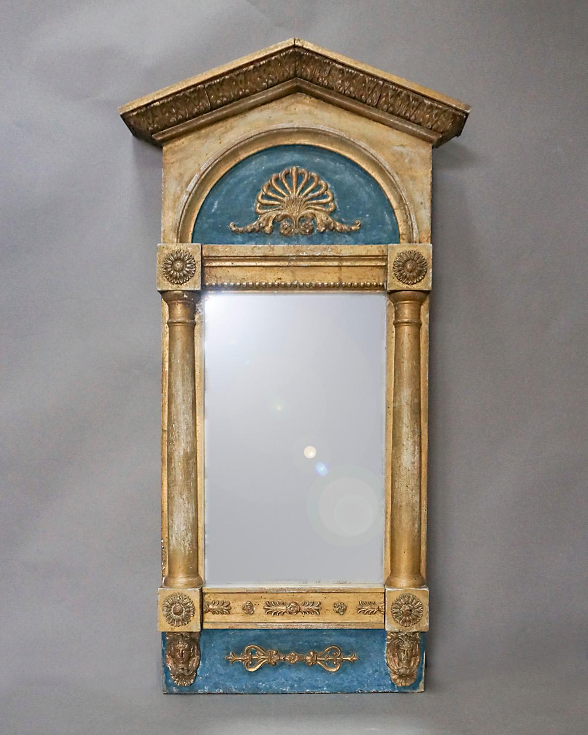 Neoclassical mirror, Sweden circa 1830, with half-columns on either side and a peaked cornice. Above and below the mirror glass are panels with gilded details against a blue background. The sunflower appliques at the corners and the Egyptian heads