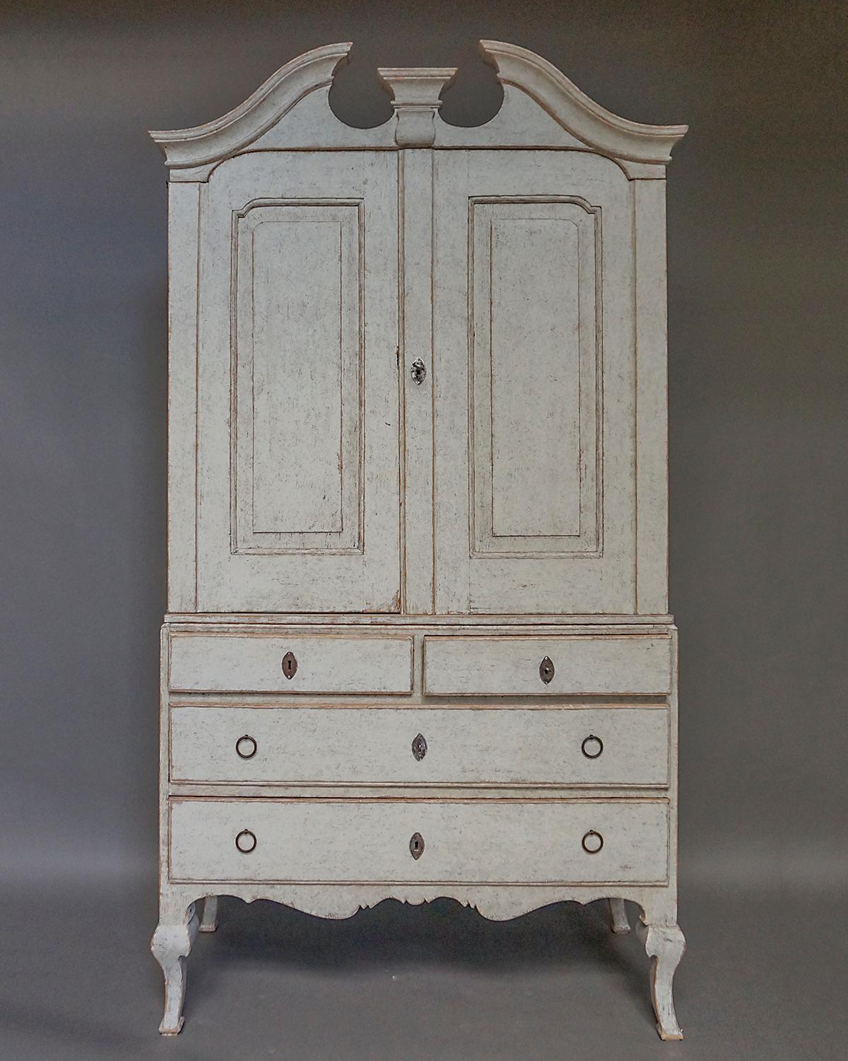 Rococo cabinet in two parts, Sweden circa 1760, with original pulls and locks. The upper section has a broken arch cornice over a pair of doors with beautifully shaped raised panels. Inside are two fixed shelves over two small drawers. The lower