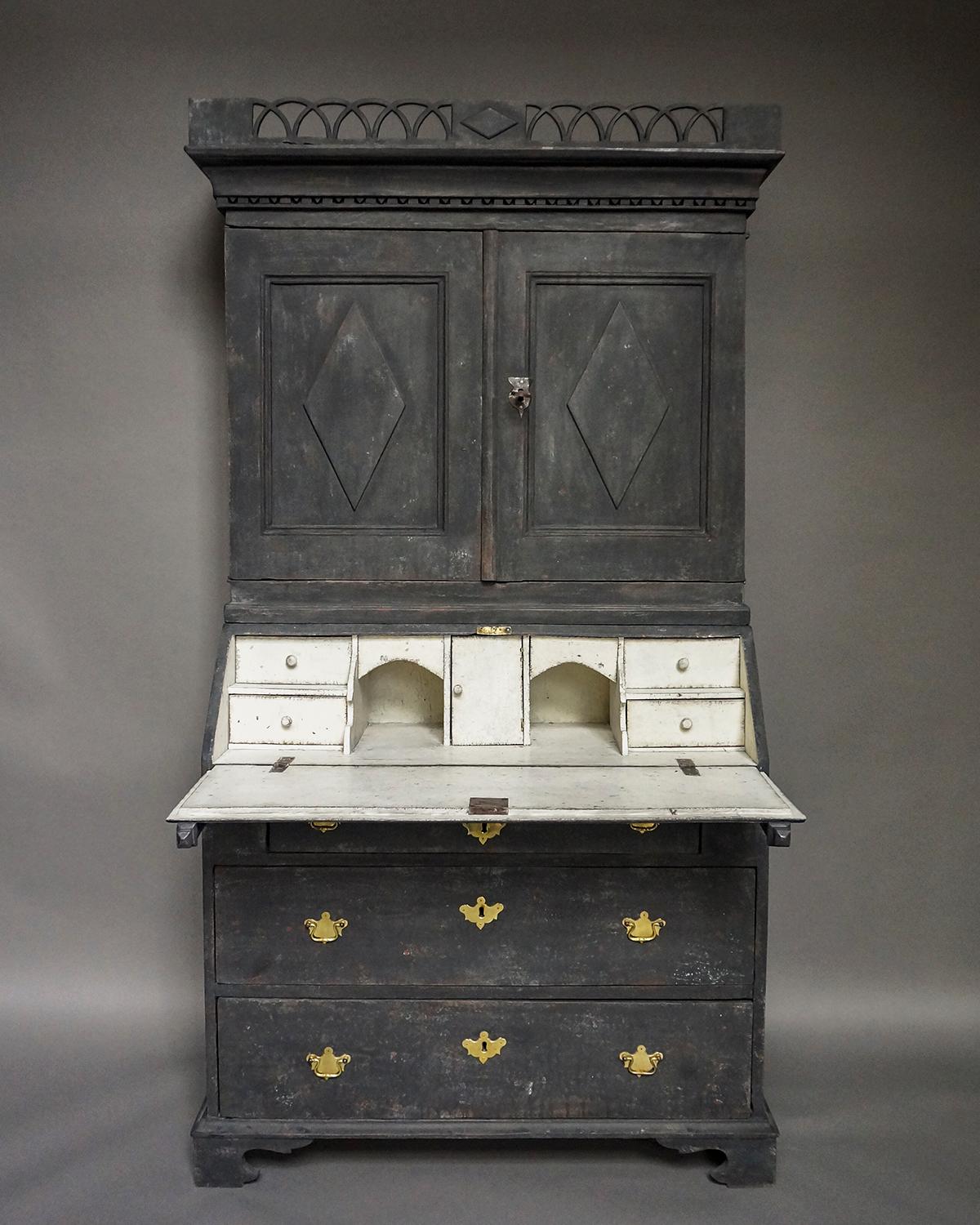Two part secretary in black paint, Sweden, early 19th century, with original lock and key. The upper section has a remarkable pierced cornice and two raised panel doors below dentil molding. The interior has three fixed shelves, the upper one with