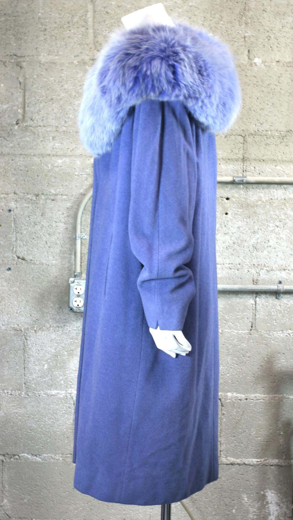 Veilchenblauer Mantel aus Wolle/Kaschmir und Fuchsfell. Erstaunlich intensive Färbungen, zum Einwickeln und Umklammern oder offen getragen werden. Der Ausschnitt ist sehr offen und der Pelz verlängert die Schulterlinie nach außen. Tiefe