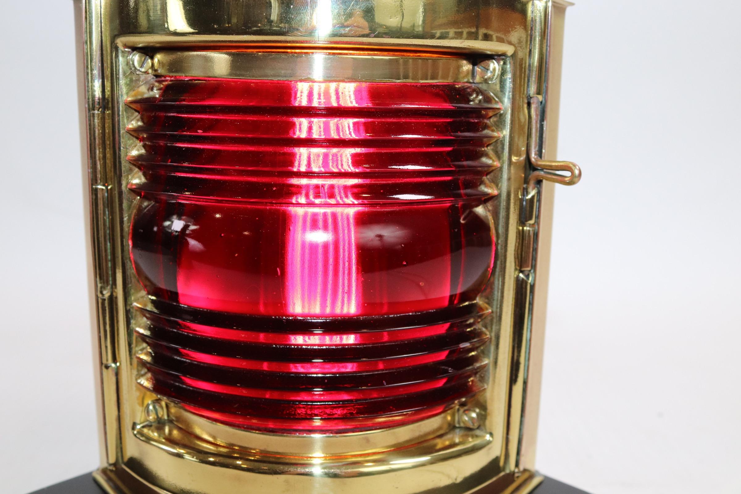 Solid brass highly polished and lacquered boat lantern by the famous Perkins Marine or Perko. With a rich red port lense, mounted to a thick wood display base with dark finish. The lantern has been wired for home use. Hinged door to front. Weight is