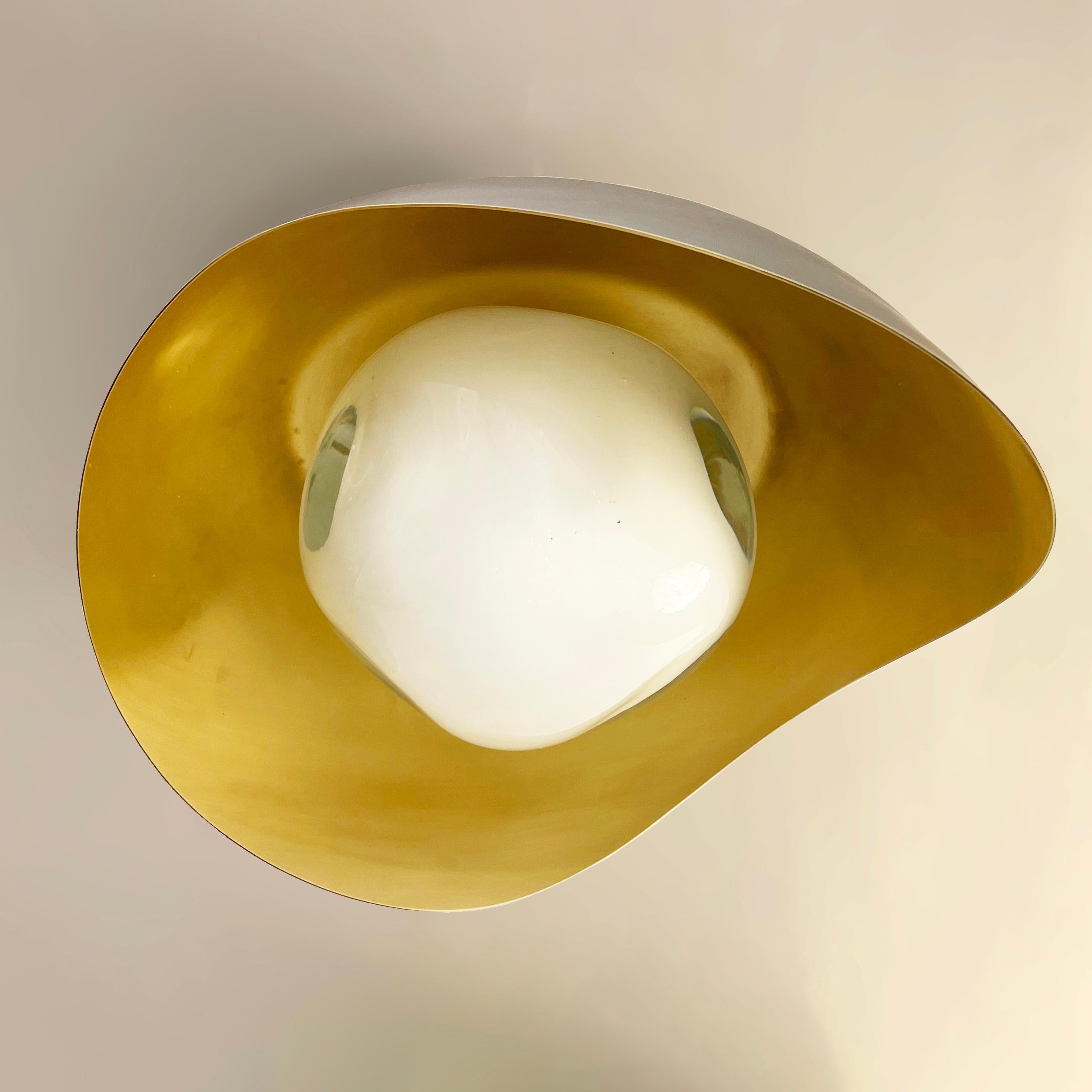 Die Leuchte Perla besteht aus einer organischen Messingschale, in die unser in der Toskana mundgeblasenes Sfera-Glas eingebettet ist. Die ersten Bilder zeigen die Leuchte mit einer Innenseite aus satiniertem Messing und einer Außenverkleidung aus