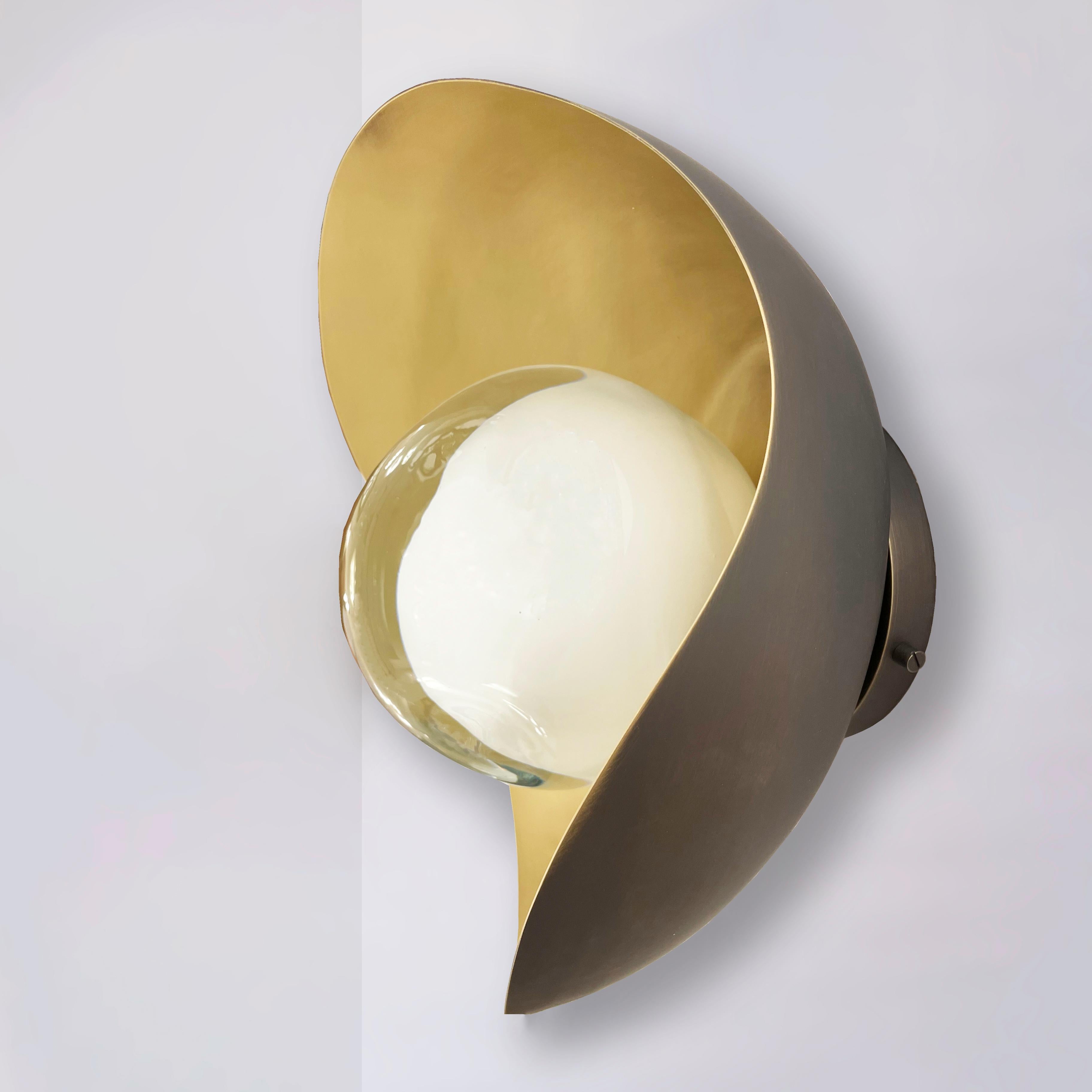 Die Wandleuchte Perla besteht aus einer organischen Messingschale, in die unser in der Toskana mundgeblasenes Sfera-Glas eingebettet ist. Die ersten Bilder zeigen die Leuchte mit einer Innenseite aus satiniertem Messing und einer Außenverkleidung
