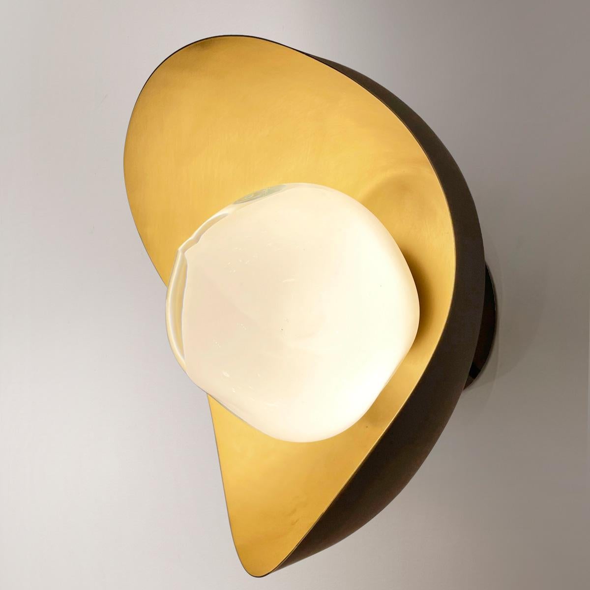 El aplique Perla presenta una concha de latón orgánico que alberga nuestro vidrio Sfera soplado a mano en la Toscana. Las primeras imágenes muestran la luminaria con un interior de latón satinado y un acabado exterior Bronzo Nuvolato (bronce); las