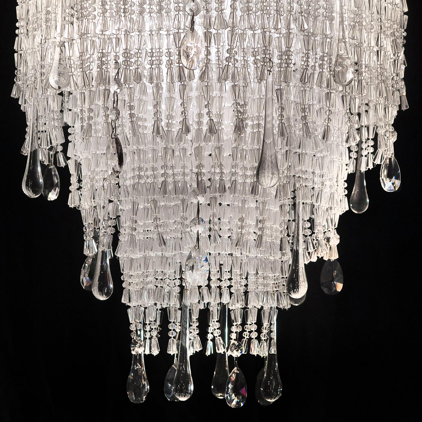 Densely embellished with precious crystal elements, this suspension lamp boasts a remarkable tiered silhouette evoking a cascade. Entirely handcrafted, it is mainly composed of clear, irregularly shaped beads in methacrylate hanging down in straight