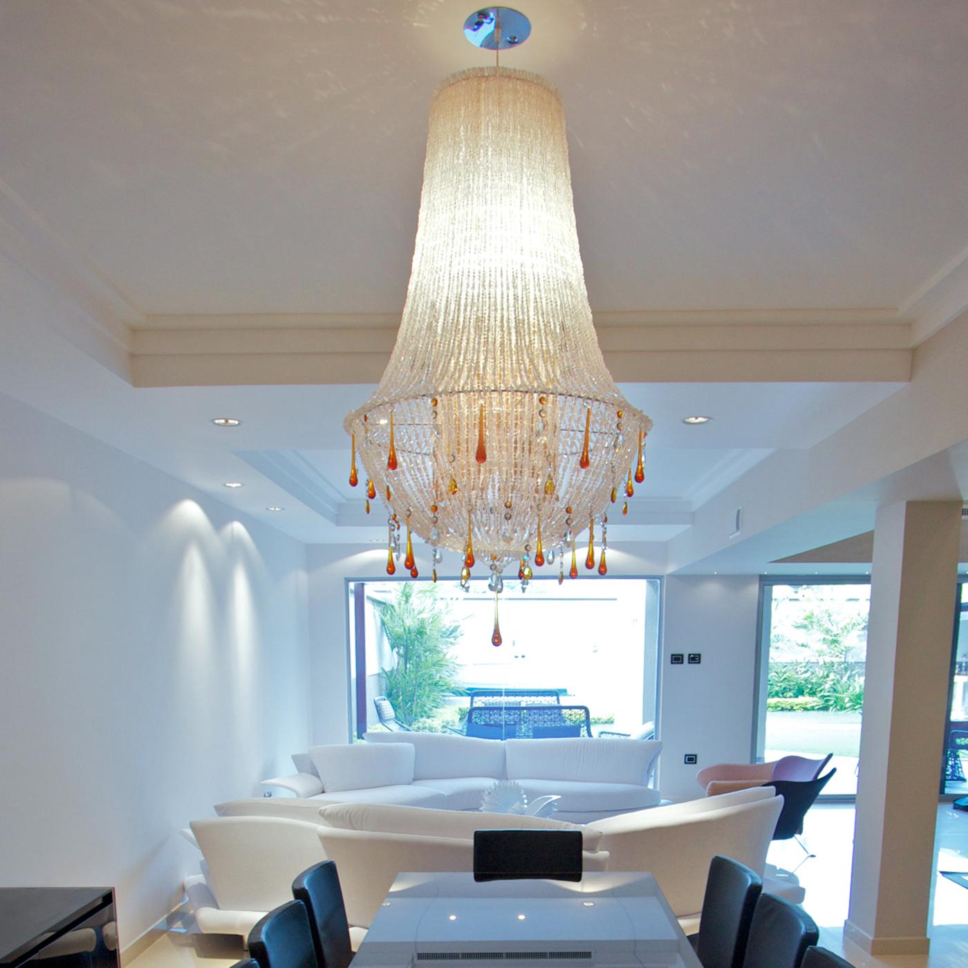 Imbuing rooms with its sumptuous yet elegant flair, this minutely handcrafted pendant lamp is distinguished by a flared silhouette made of strands of transparent beads in methacrylate and prized, teardrop-like pendants in amber-colored glass and