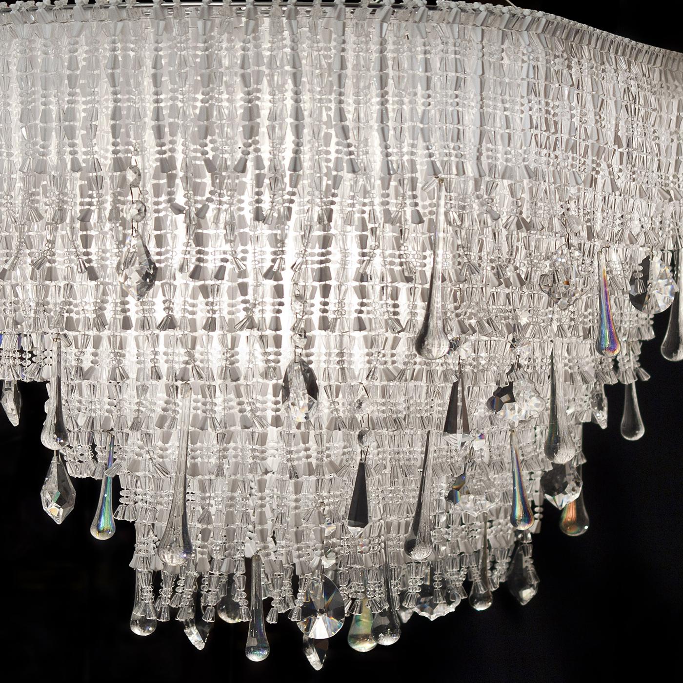 Questa elegante lampada a sospensione ellittica, dal design unico che spicca negli interni più raffinati, è caratterizzata da una cascata di perle acriliche ed elementi in cristallo trasparente minuziosamente legati a mano. Caratterizzato da una