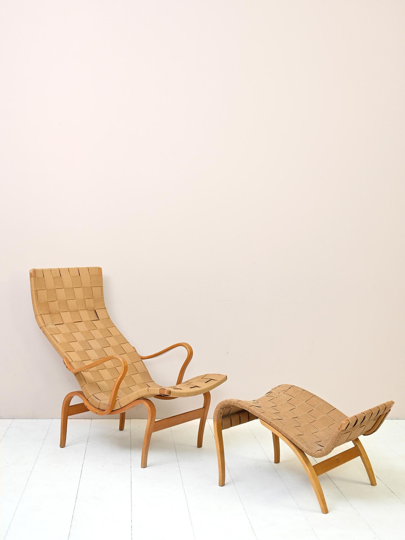 Iconic 'Pernilla' armchair and footstool designed by Bruno Mathsson for Karl Mathsson AB in Värnamo, Sweden in the 1940s.

The frame is made of birch wood and the seat of canvas with crossed straps.

Good condition. The color of the canvas of