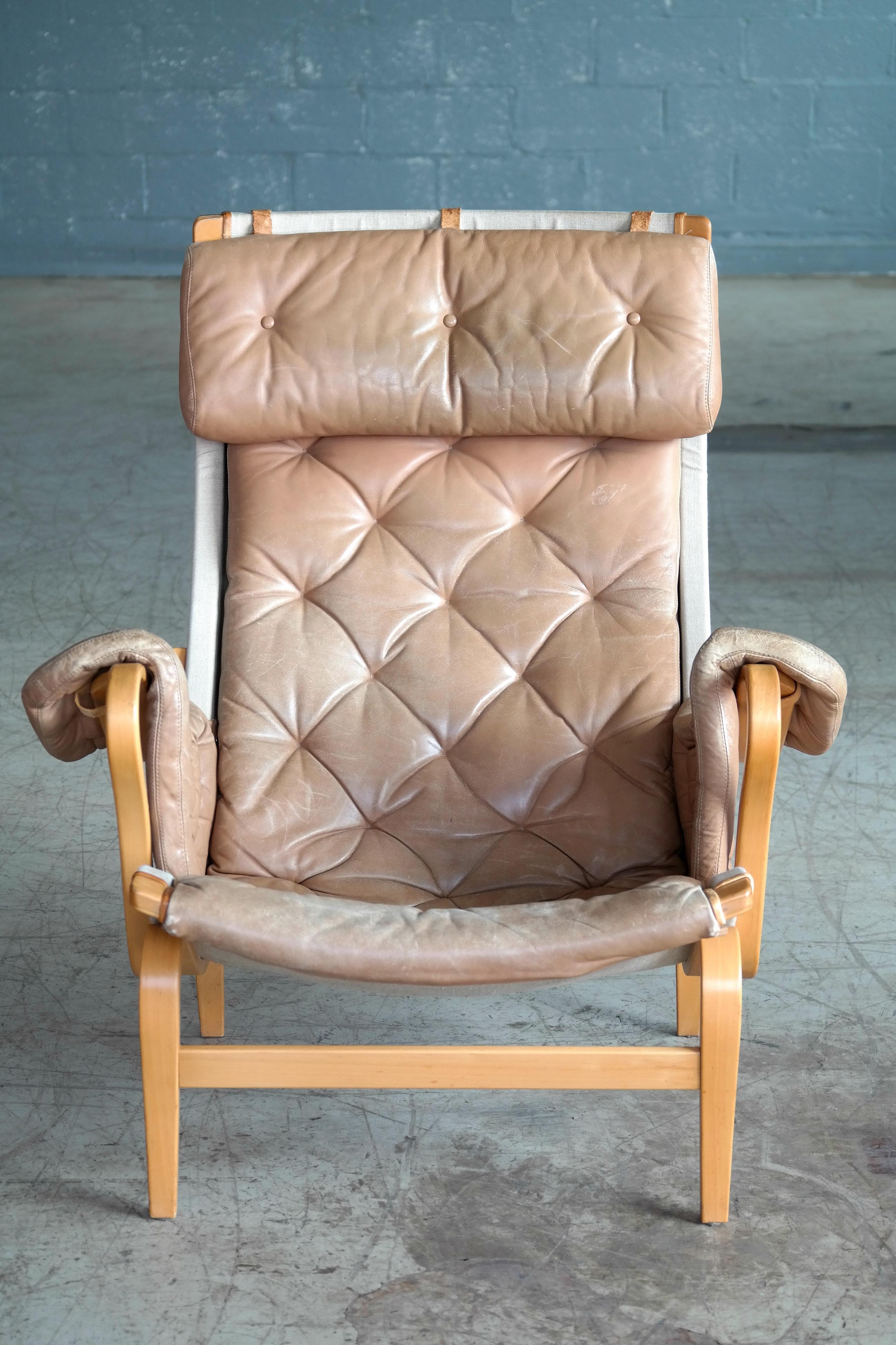 Wonderful Pernilla chair by Bruno Mathsson for DUX, composed of a tufted camel color leather cover on canvas on a molded beech plywood frame, with adjustable leather headrest on leather straps. One of the most comfortable chairs ever made and super