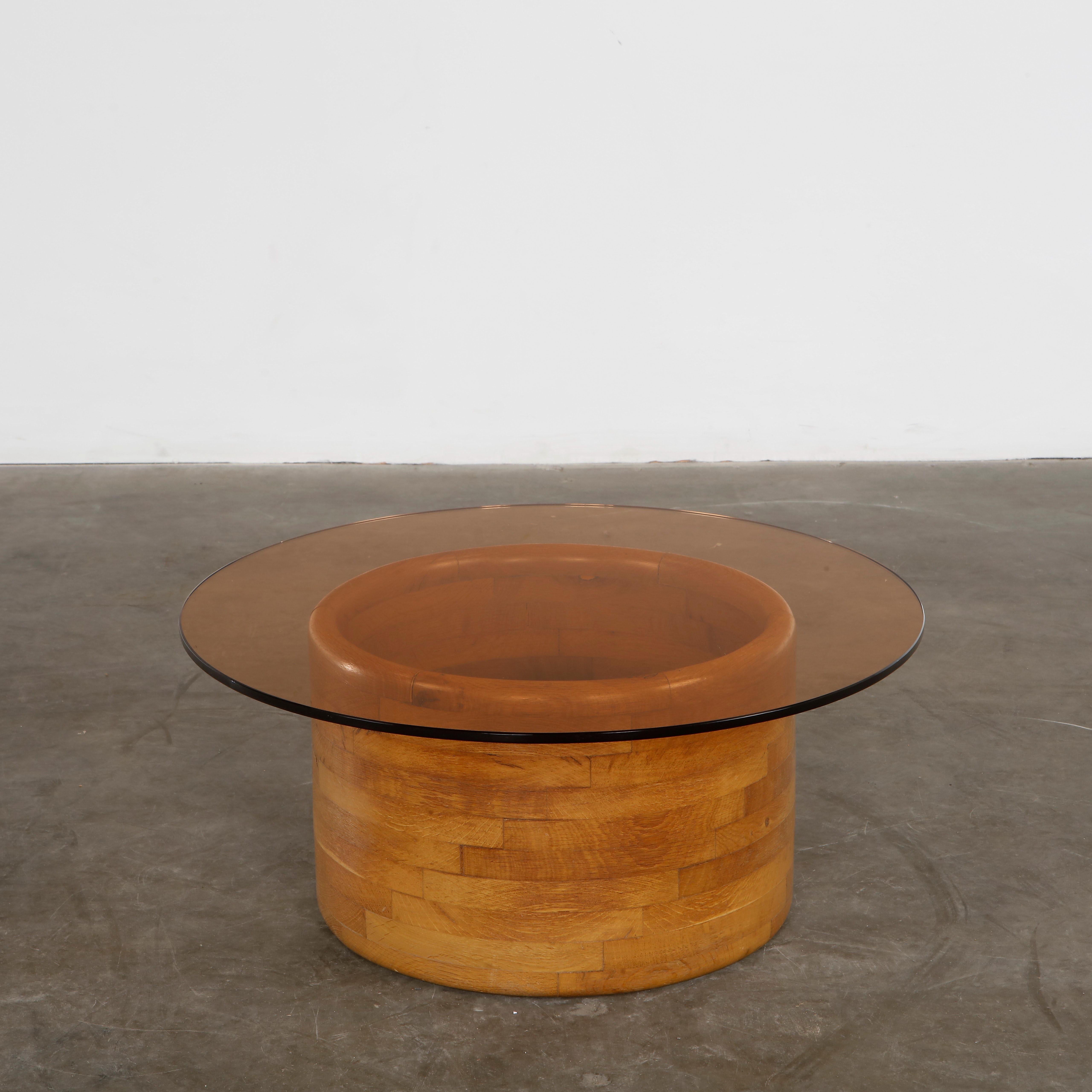 Mesa de centro en forma de tambor con tapa de cristal ahumado y base de madera. Escultural y cálido, perfecto para espacios inspirados en los años 70. Altura: 12,1 pulg. Diámetro: 28 pulg.