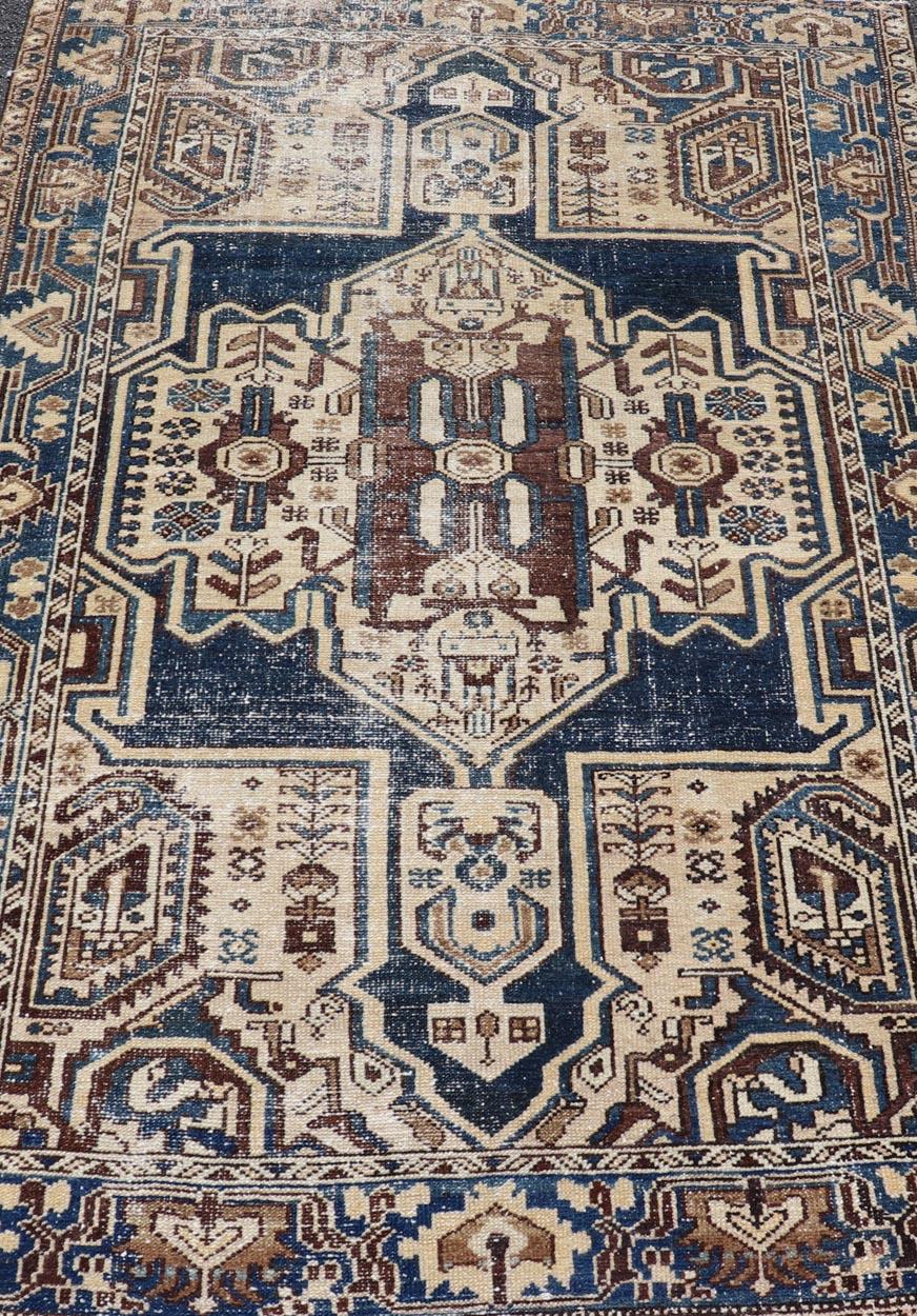 Measures: 4'4 x 6'9 
The rug's central field showcases a prominent medallion pattern set against a deep blue background, accented with beige and brown geometric and floral motifs. The medallion itself is highly detailed, featuring a complex