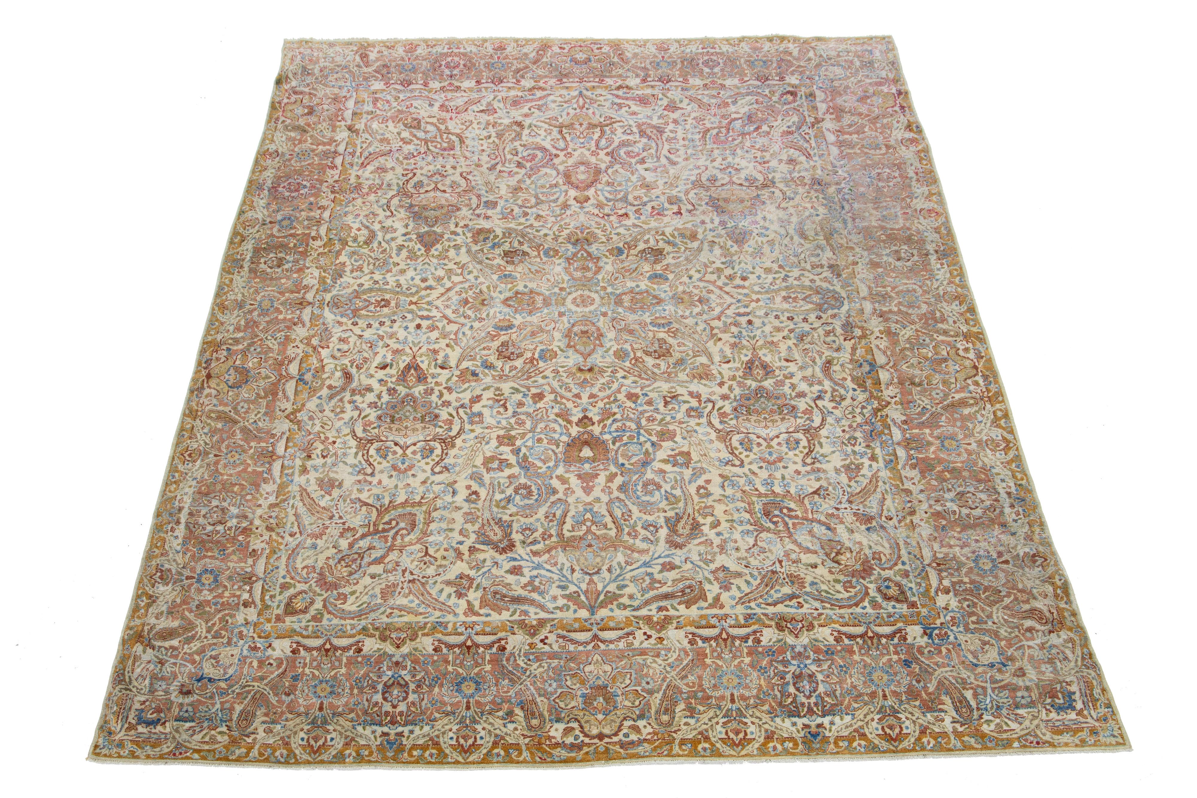 This exquisite, hand-knotted wool rug from Kerman boasts a charming antique finish. The rug's warm beige-tan color field is adorned with a stunning, all-over floral pattern, highlighted by hints of rich blue and rust—a remarkable piece of Persian