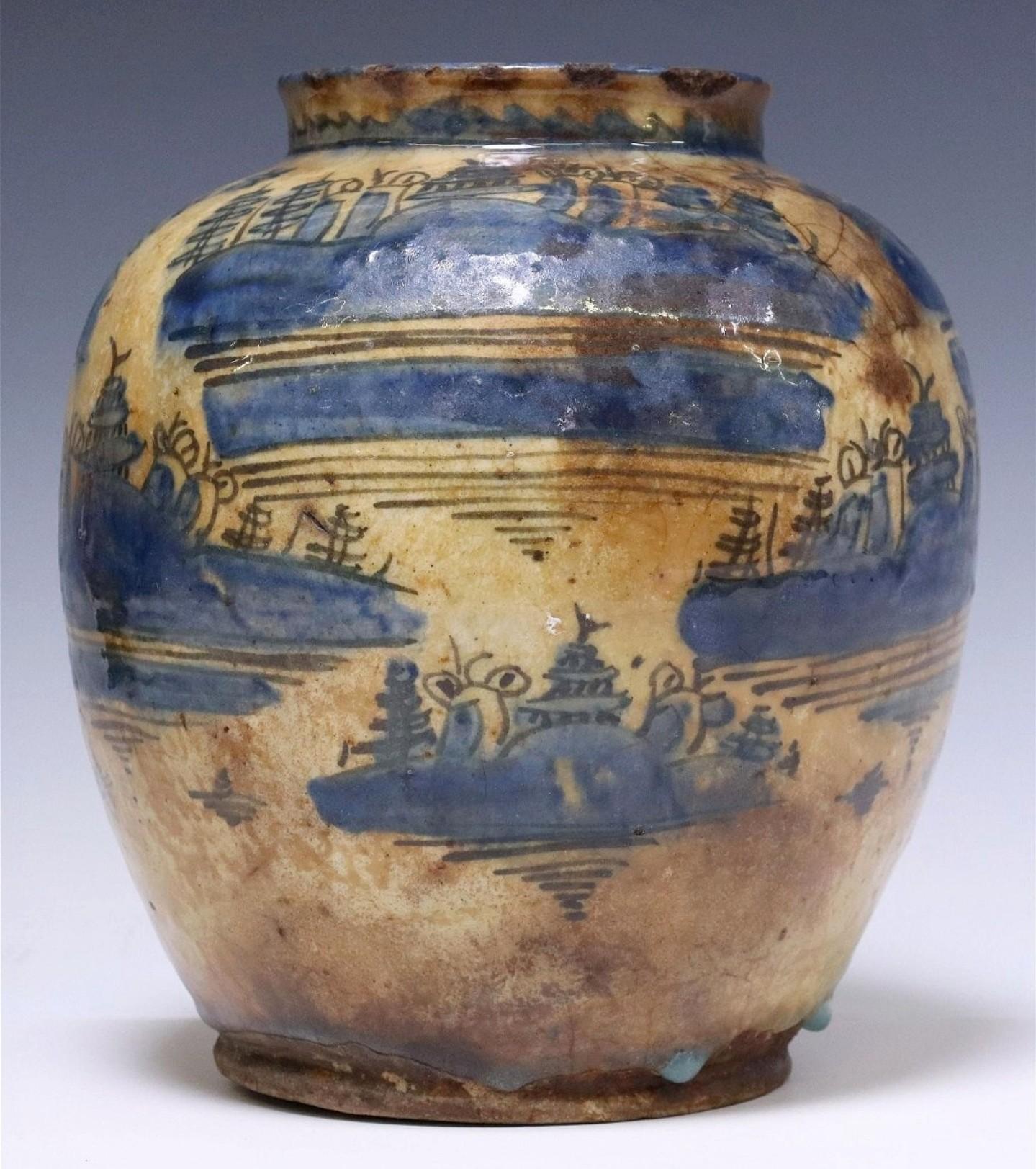 A scarce Safavid dynasty (1501-1736) blue and white glazed earthenware pottery jar or vase, circa 1600, Persia, having a tapered body, cream ground with blue underglaze and hand-painted Islamic architectural landscape motifs. 

Dimensions: (approx)