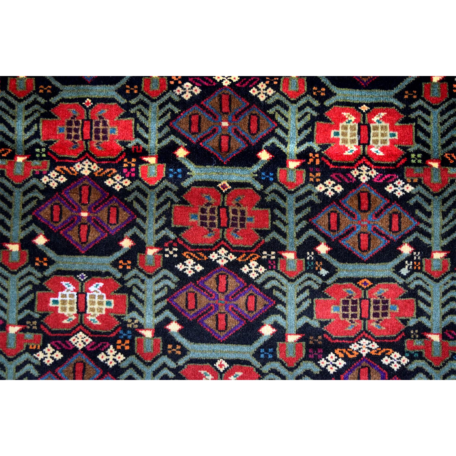 Ce tapis persan Balouchi en laine filée à la main et teintures végétales, datant de 1950, présente un motif géométrique complexe avec de multiples bordures et une coloration unique de rouges chauds et de roses froids, de bleus et de verts. Alors que
