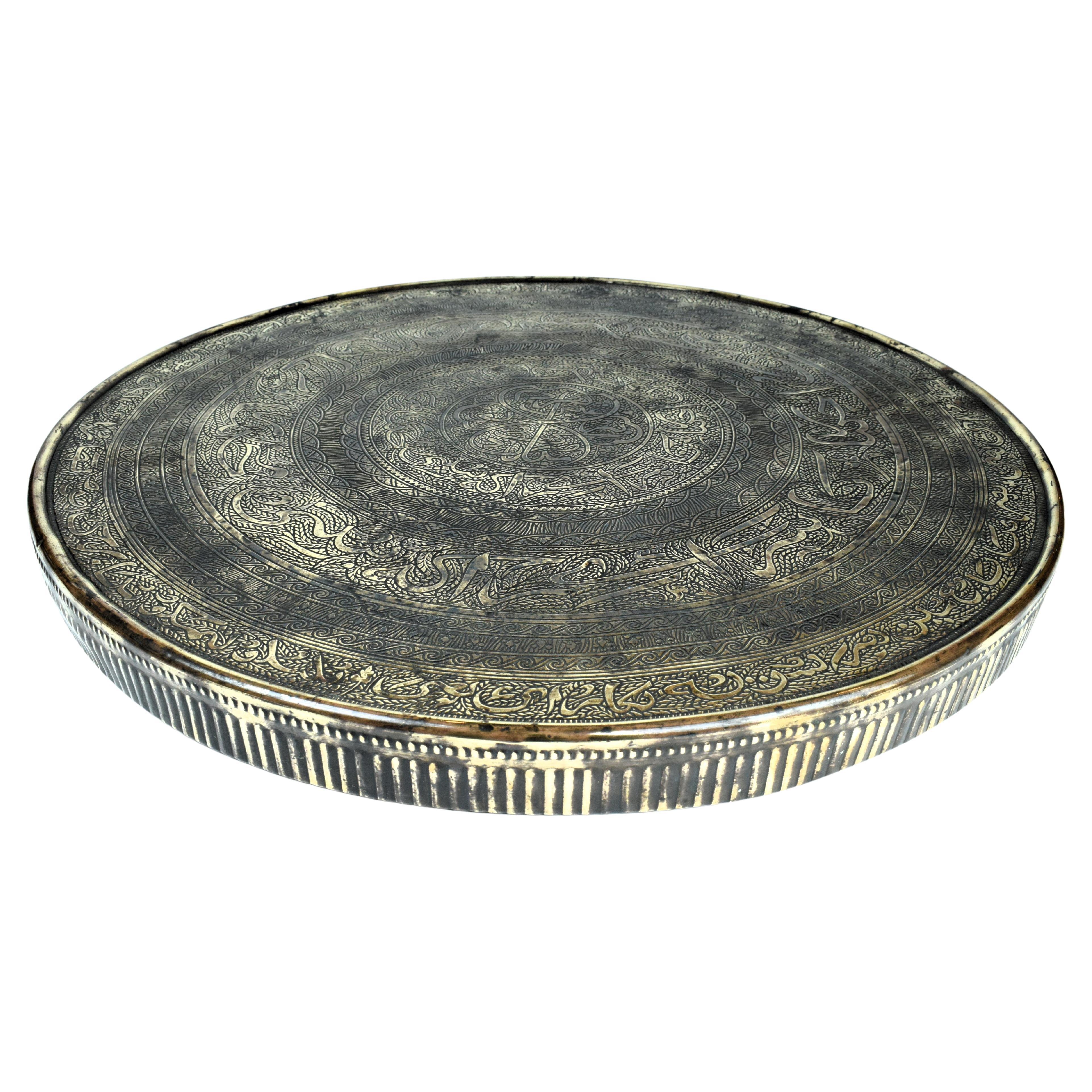 The Persian brass round platter from the early 20th century is a stunning example of Persian metalwork, showcasing a fusion of calligraphic and geometrical engravings. This platter crafted by skilled artisans, reflects the cultural and artistic