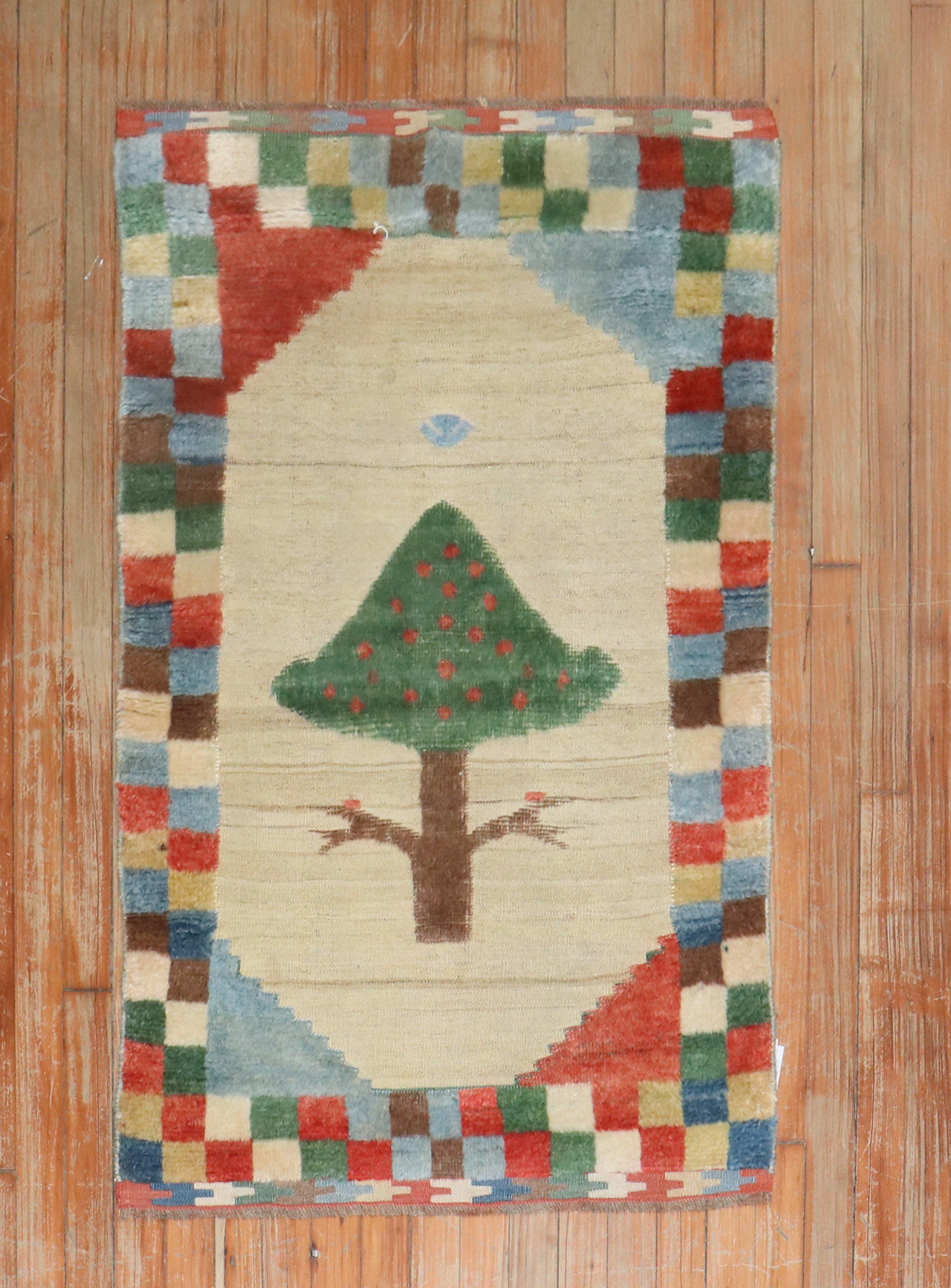 Gabbeh-Teppich aus dem späten 20. Jahrhundert mit einer bunten karierten Bordüre, umgeben von einem freistehenden Baum auf Kamelgrund, gewebt in Souf-Technik

Maße: 2'6'' x 3'11''

Souf-Teppiche sind eine sehr selten anzutreffende Technik, da sie