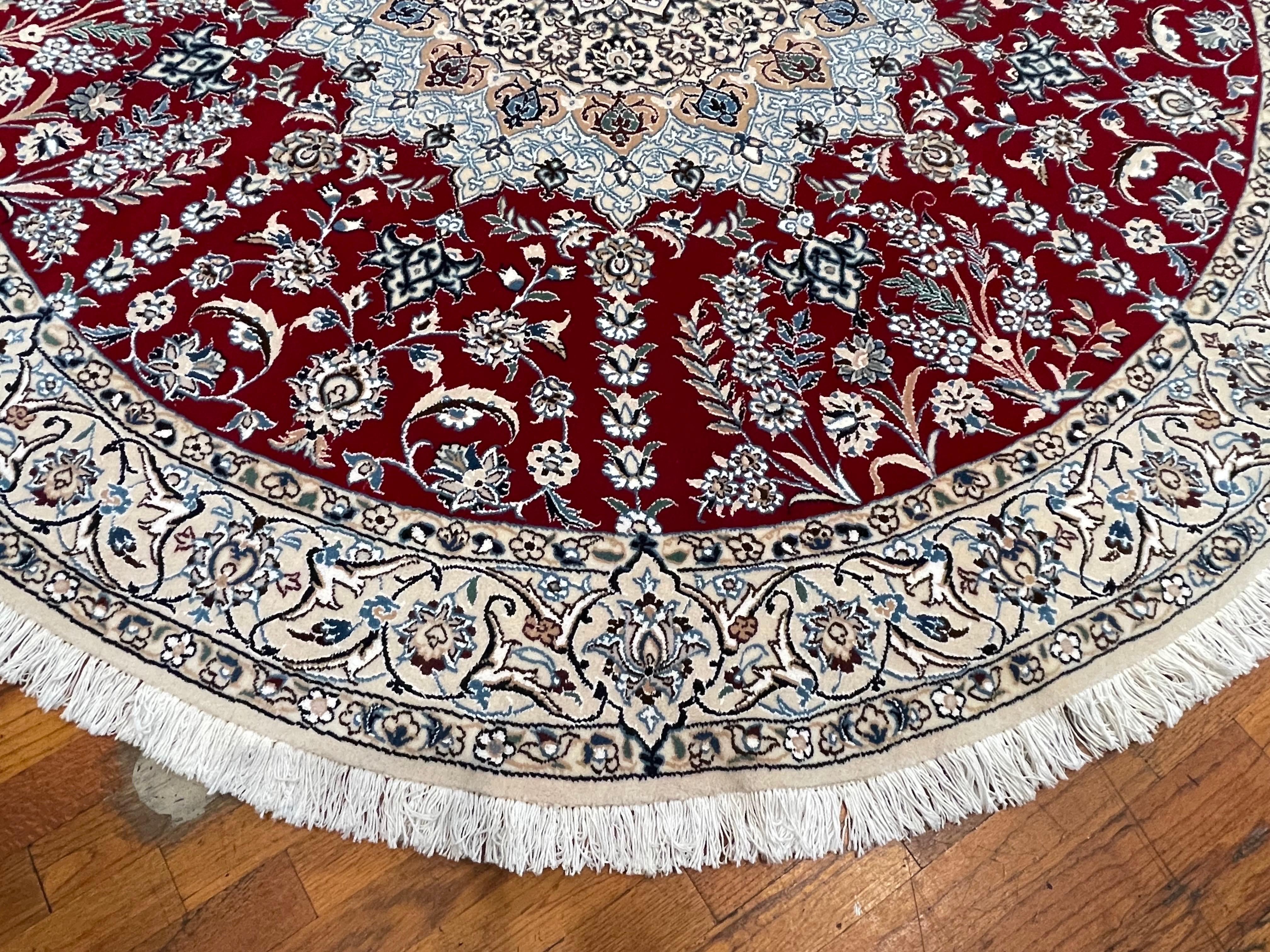 Cet authentique tapis persan rond de Nain (9 LA), fait à la main, est composé de poils de laine et de soie et d'une base en coton. Nain est une ville d'Iran réputée pour sa production de tapis artisanaux. Ce tapis présente un médaillon central avec