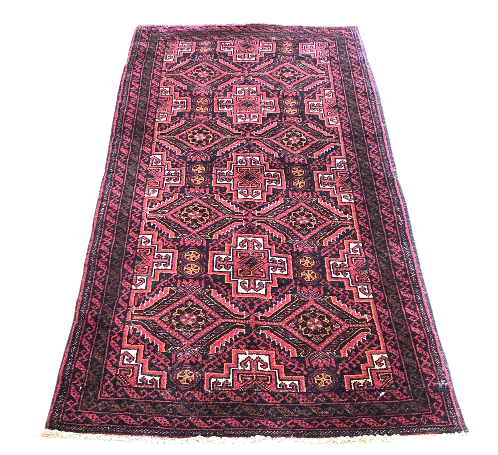 This authentic Persian Baluchi rug has wool pile and foundation which are hand-knotted by the nomads of Baluchi. The age of this rug is almost 50 years old. The base color and border colors are red. The size of this rug is 2 feet 7 inches wide by 5