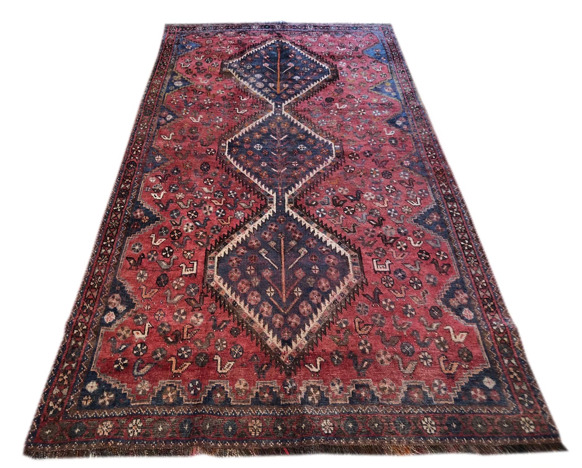 This colorful Shiraz rug has nomadic patterns with repeated medallions. Both Pile and foundation are wool. This rug has geometric birds and flower motifs all over the rug. The base color is red with the combination of blue, salmon, taupe and cream.