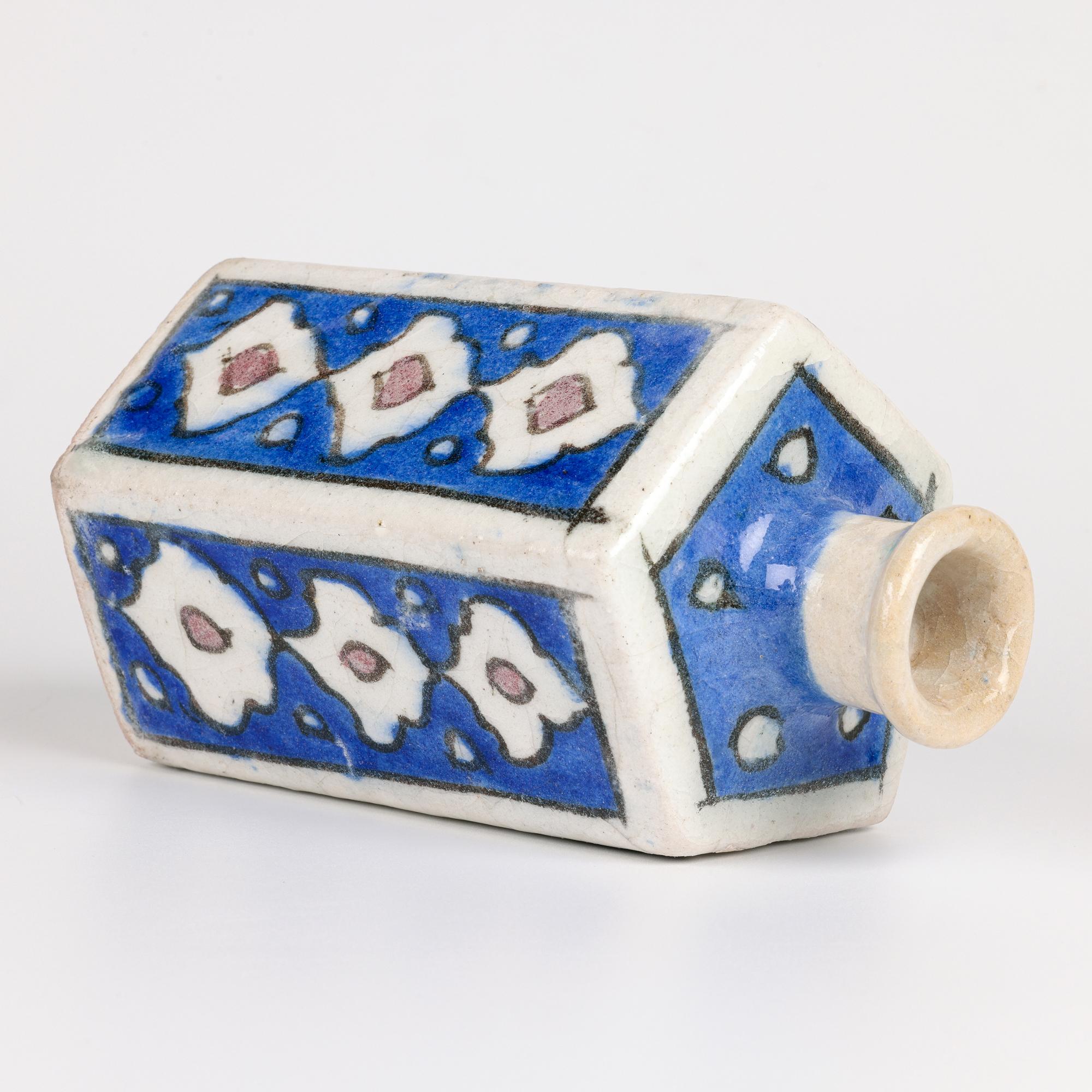 Issu d'une petite collection de cinq vases en poterie persane peints à la main, cet élégant vase en faïence à cinq côtés (en forme de polygone) en forme de bouteille, peint à la main avec des motifs de panneaux de feuilles stylisées, date du début