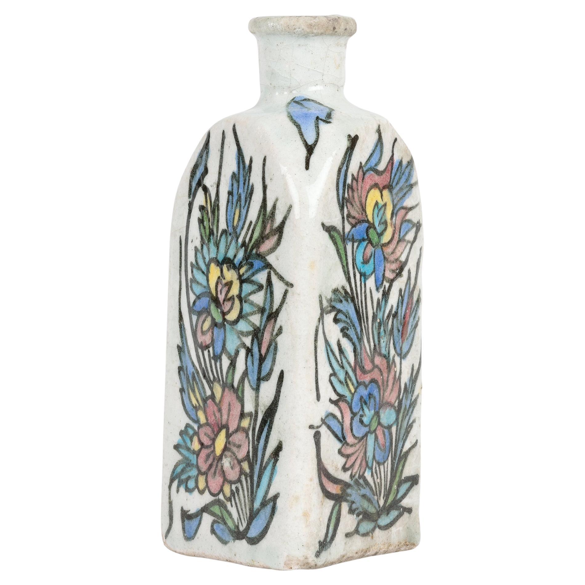Issu d'une petite collection de cinq vases en poterie persane peints à la main, cet élégant vase triangulaire en faïence peint à la main d'un oiseau au milieu de tiges fleuries date du début ou du milieu du 20e siècle. Le vase à trois faces est