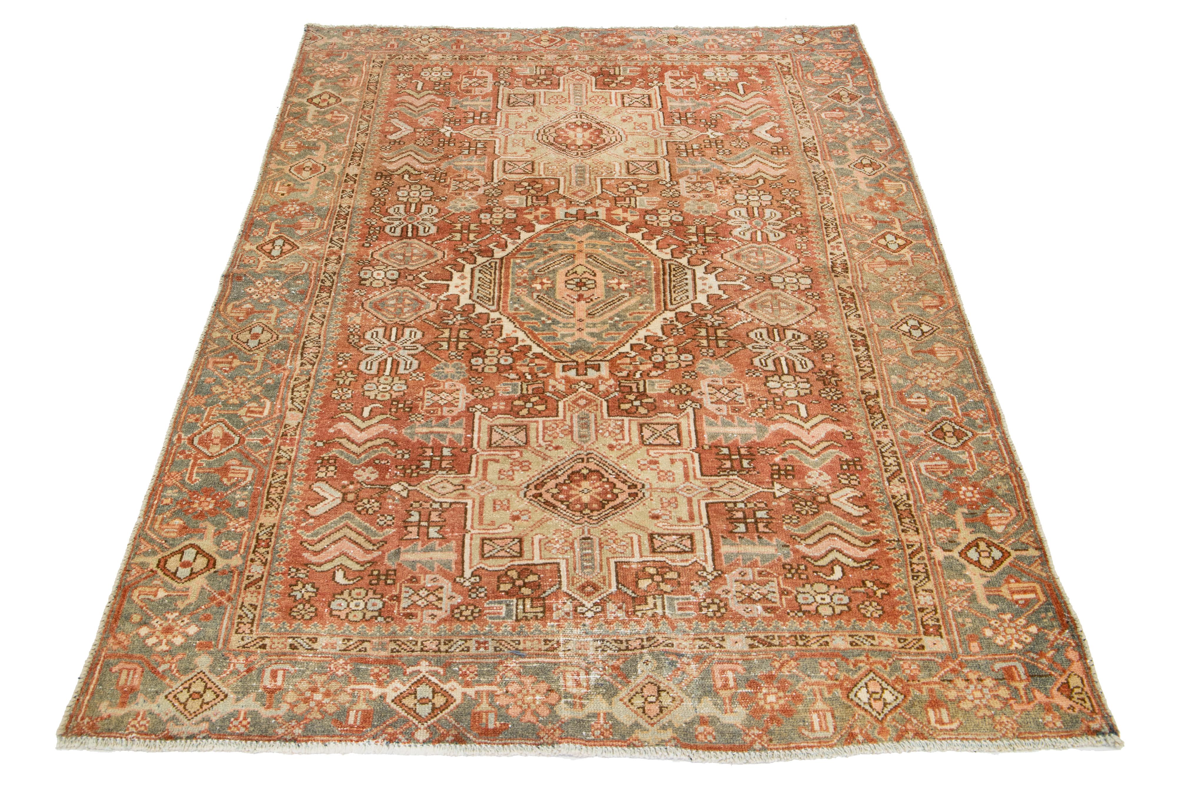 Dieser antike persische Heriz-Teppich ist aus handgeknüpfter Wolle gefertigt. Das rostorangefarbene Feld zeigt ein fesselndes Tribal-Muster, das mit Beige-, Pfirsich-, Grau- und Brauntönen verziert ist.

Dieser Teppich misst 4'6