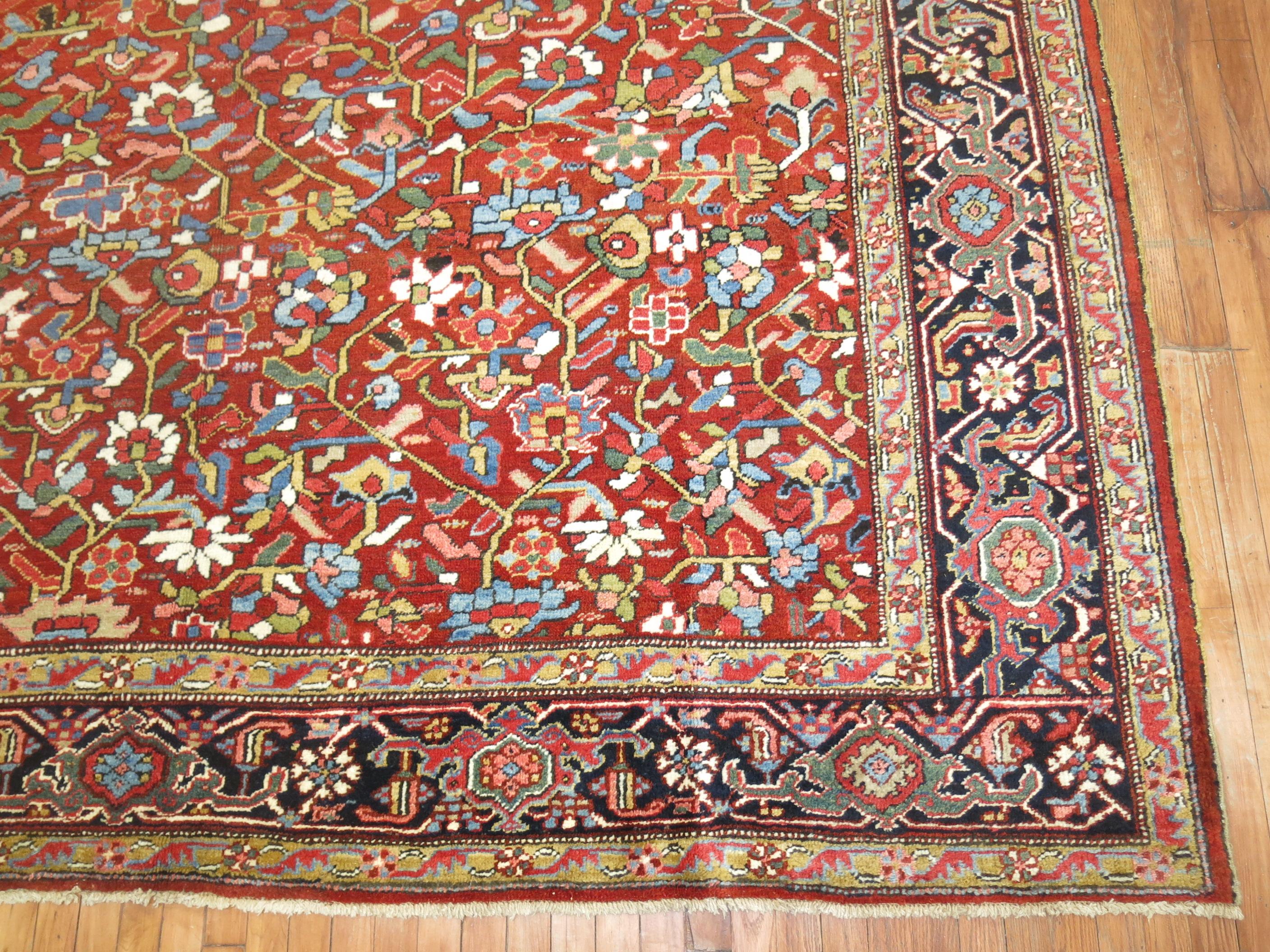 A room size antique Persian Heriz rug featuring a vivid red field with a slew of colorful accents and a navy border. The all-over repetitive design is uncharacteristic from the medallion formats made from this region, circa 1930.

Size: 9'8” x