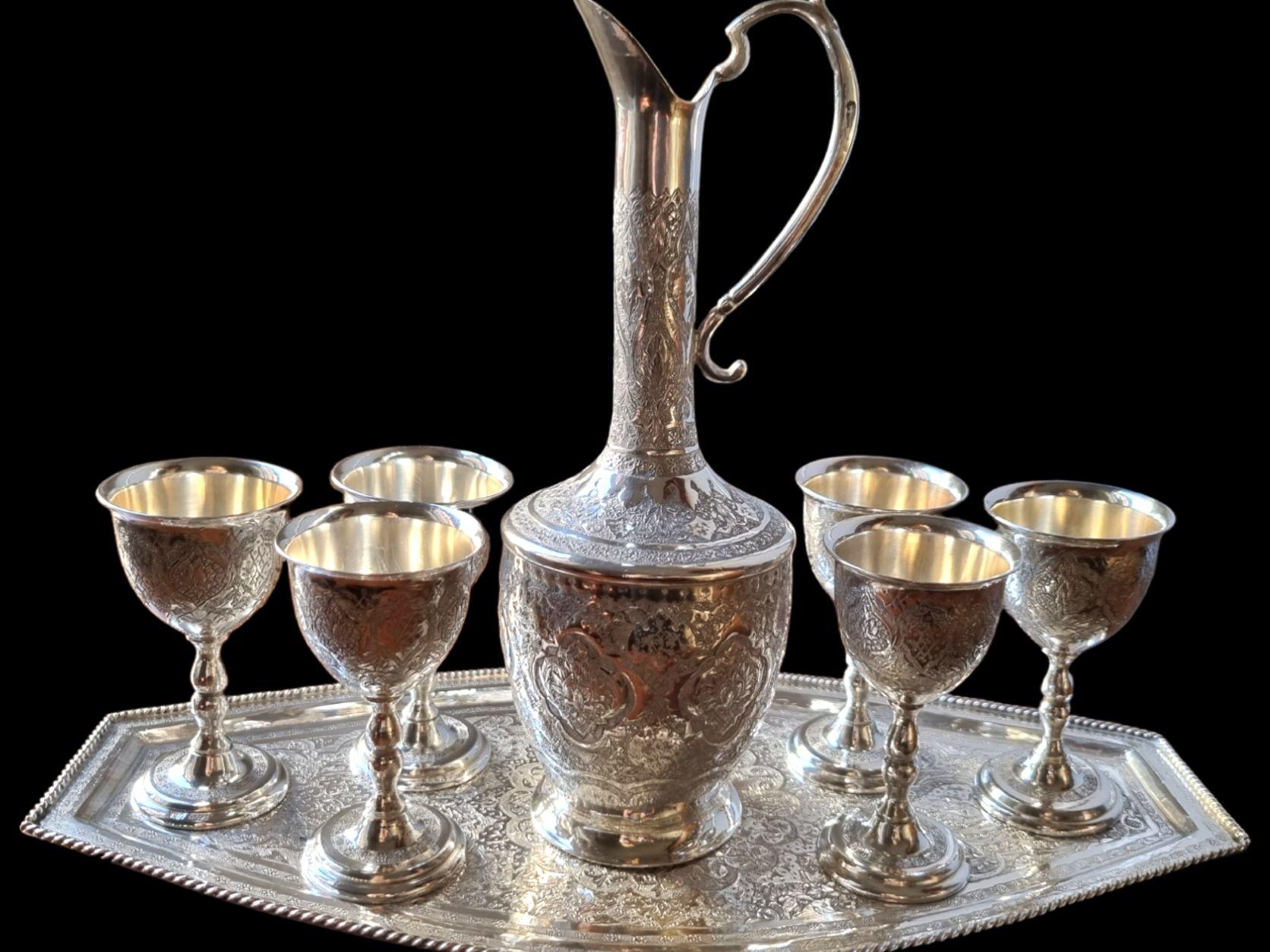 First Half 20th Century Persian Islamic Solid Silver drinking set, comprising of a Jug and six goblets on a tray, each piece profusely engraved and chased with typically Persian arabesque decoration, the jug has a long sinuous neck and cast