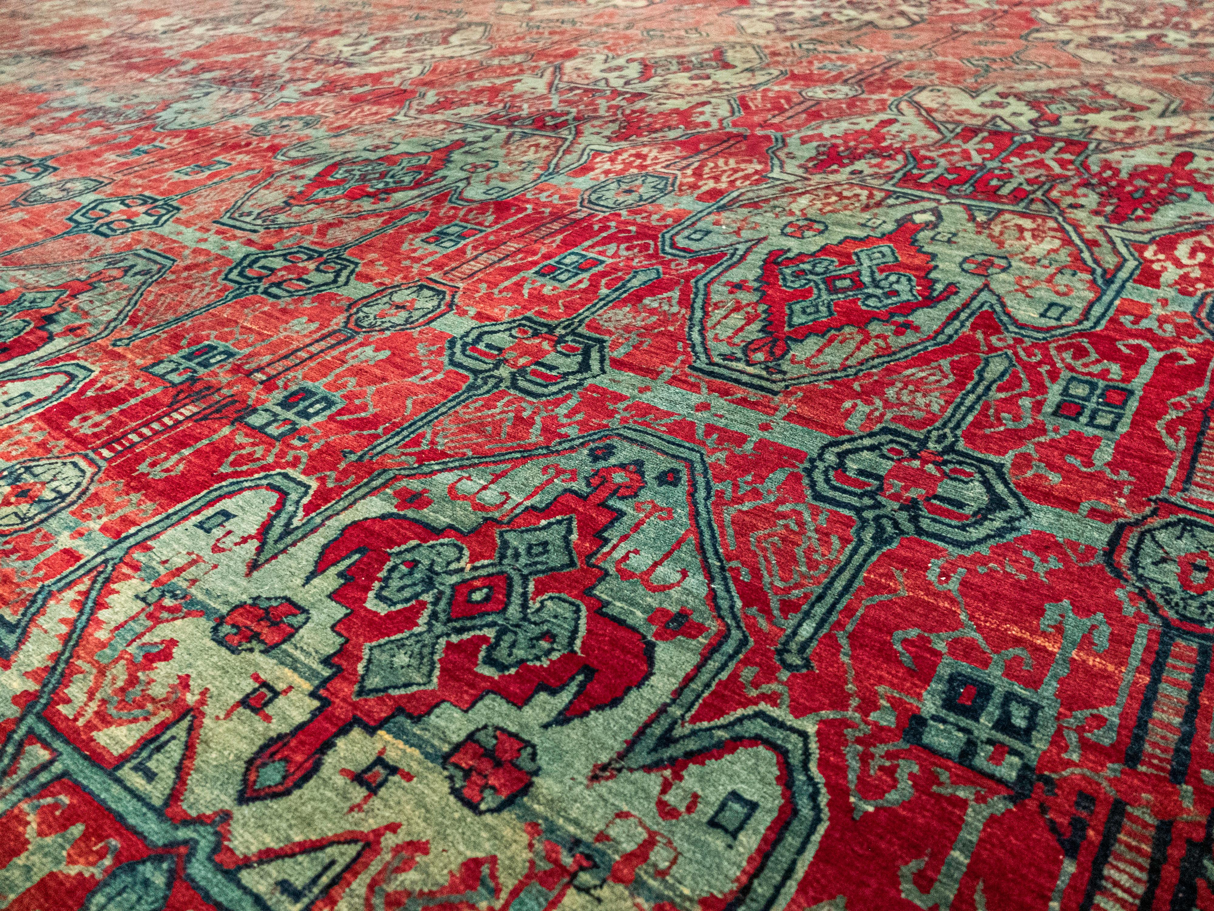 This is a uniquely patterned antique Khorasan Rug. It has intricate detailing in the main field and uses deep reds, and light greenish blues. It then has a slightly contrasting vine patterned border with pops of yellow. These specific dyes are known