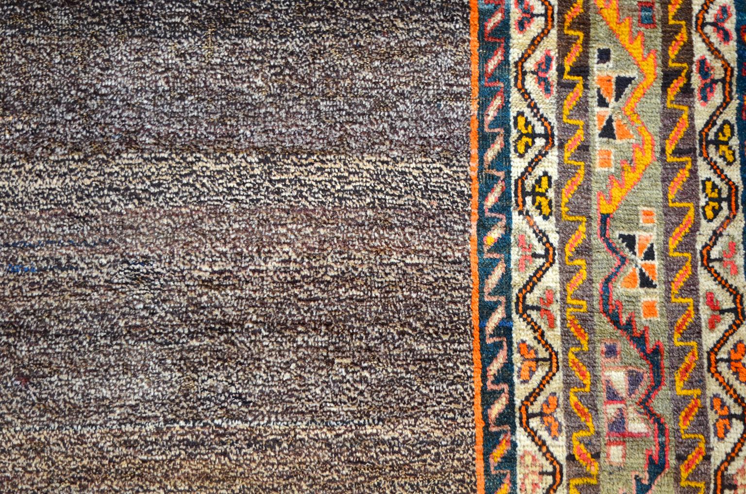 Esta alfombra persa Loristan Gabbeh de lana, de hacia 1910, consta de urdimbre de lana hilada a mano, trama y pelo anudado a mano. Los ricos colores naranjas y rojos de la lana teñida con tintes vegetales del borde llaman la atención, pero el campo