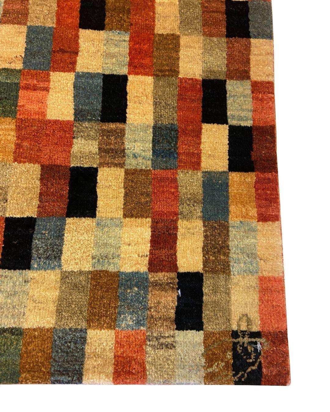 Dieser 2′5″ × 2′6″ große handgeknüpfte Perserteppich ist ein lebendiges Mosaik aus Farbe und Geometrie. Im Iran aus handgesponnener, pflanzengefärbter Wolle gewebt, wechselt die schachbrettartige Komposition zwischen warmen Rot-, Gold- und