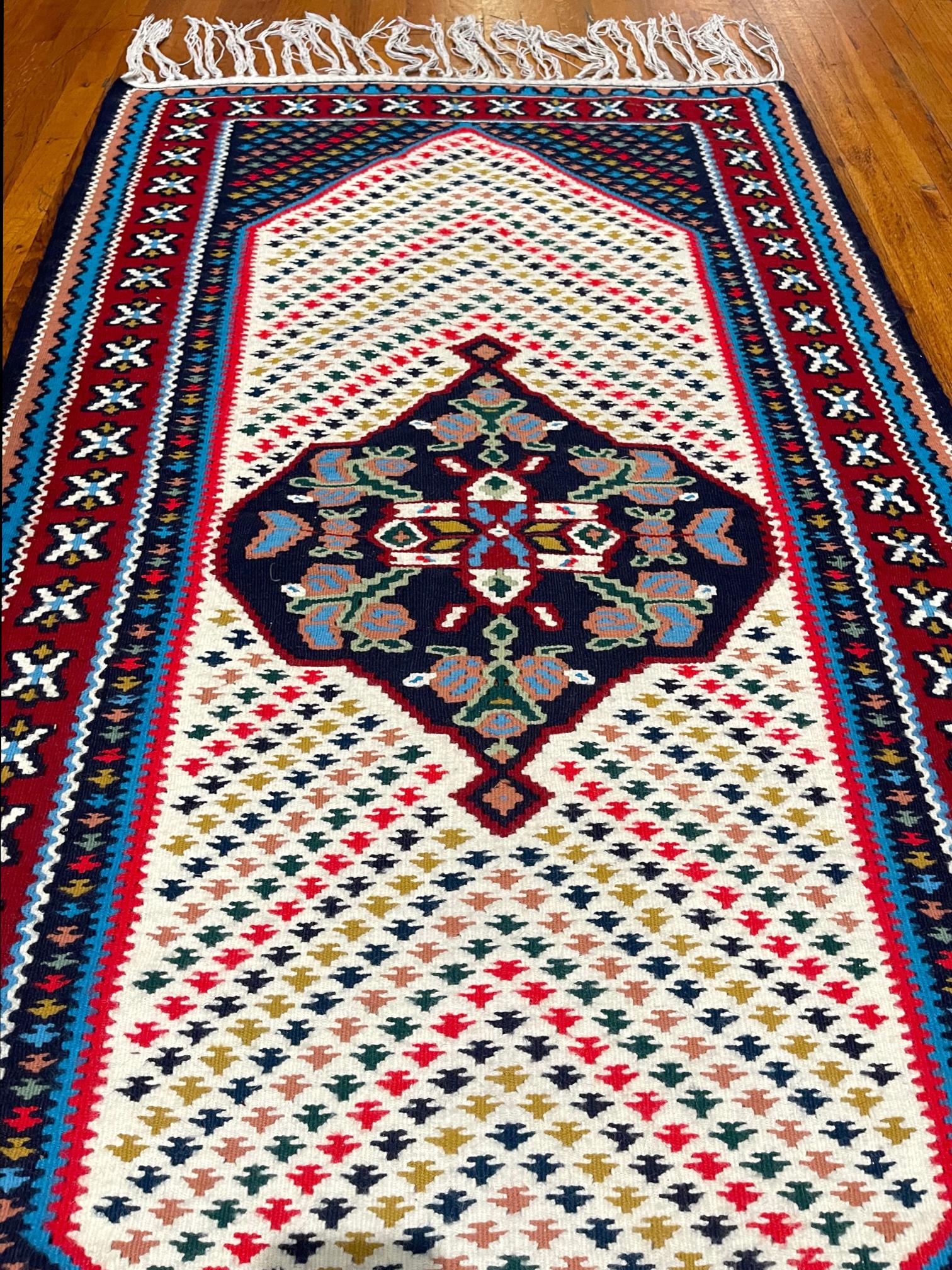 This rug is a Persian Shiraz Kilim which is a type of brocading or flat-woven pile. This is flat weave is very sturdy and reversible. The pile is with cotton foundation. The design is geometric with fish pattern.  The base color is cream and the