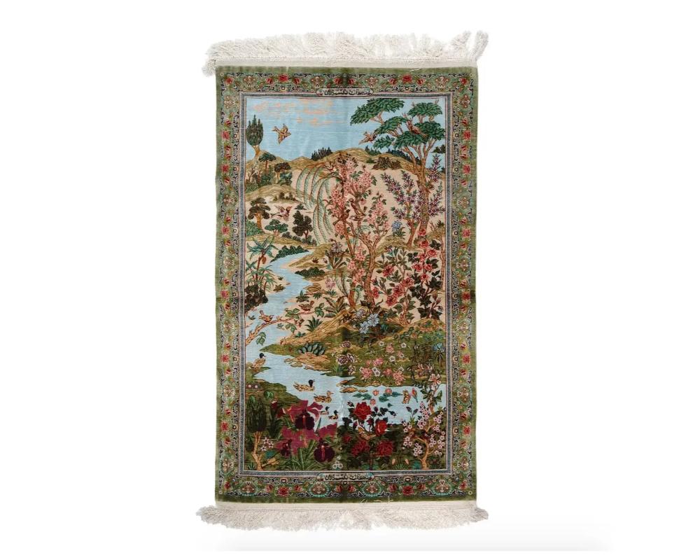 A very picturesque and skillfully hand knotted Qum Persian silk carpet by Rajabian. The carpet depicts an idyllic landscape with ducks swimming in a stream, flowers and trees on the banks and birds flying in the sky. The border is decorated with