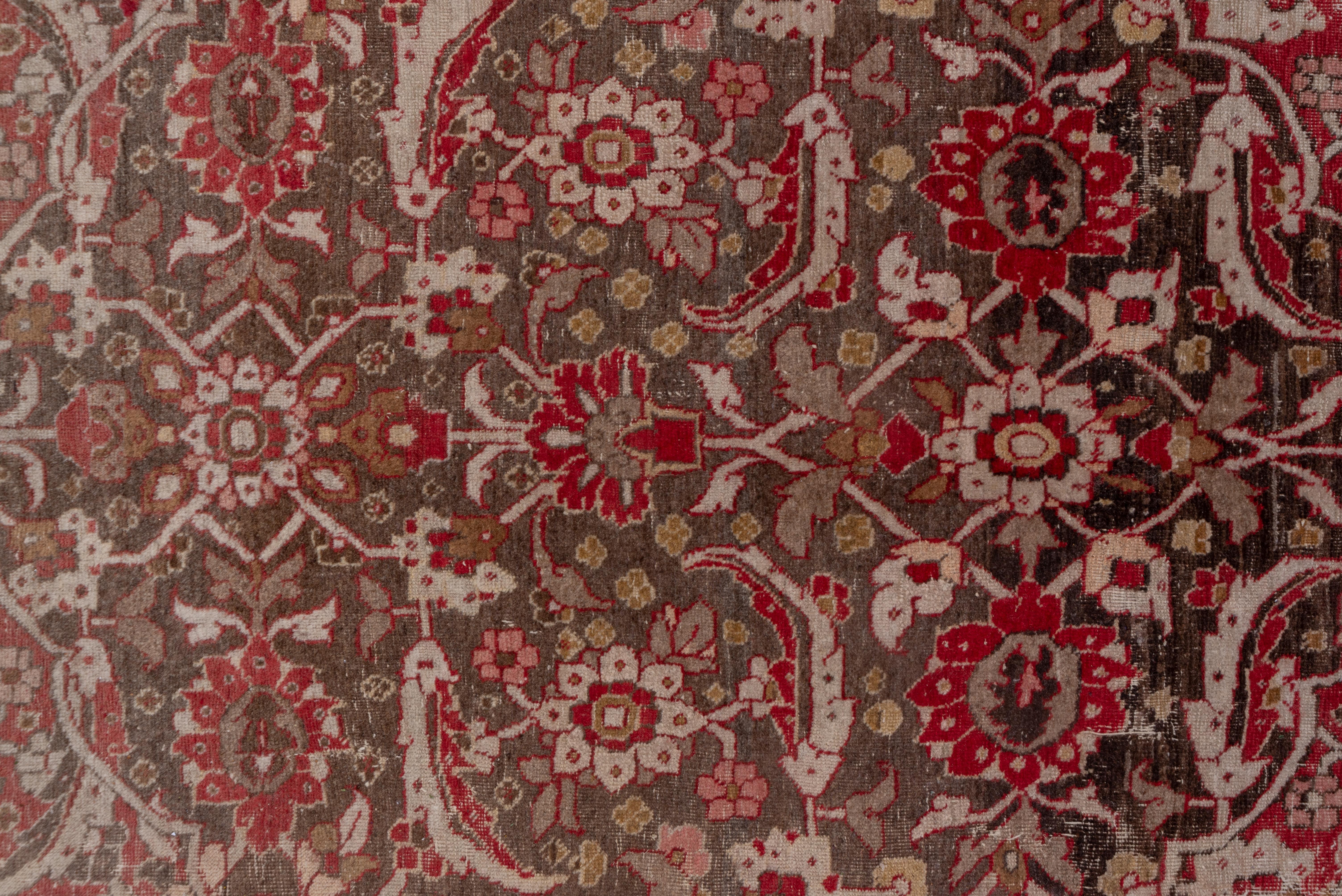Ce tapis persan bien tissé de l'entre-deux-guerres a encore de la présence dans le champ fortement abrasé qui passe de la couleur brique au brun clair avec un fort motif d'arabesques et de palmettes fleuries contenu par une rosette festonnée et des