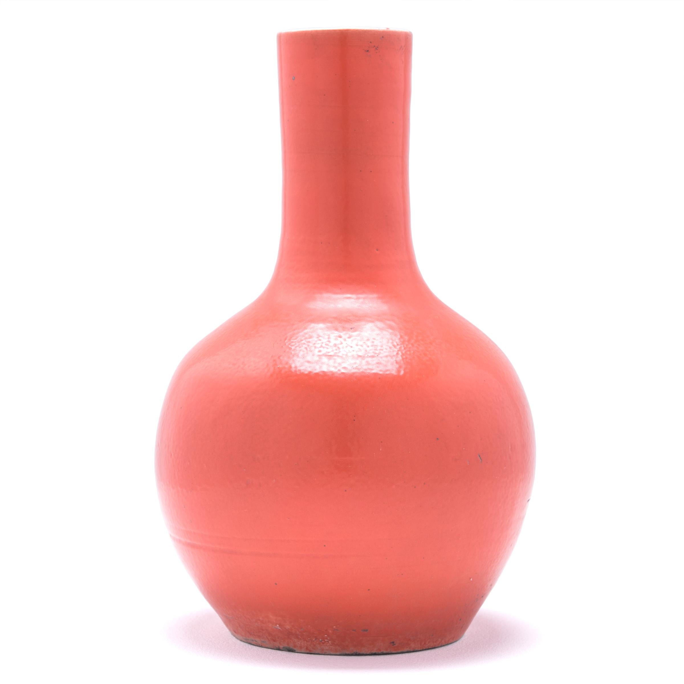 Drawing on a long Chinese tradition of monochrome ceramics, this tall gooseneck vase is glazed in vibrant persimmon-orange glaze. The vase features a rounded, globular body and a narrow cylindrical neck, a classic form known as 'tianqiuping' or