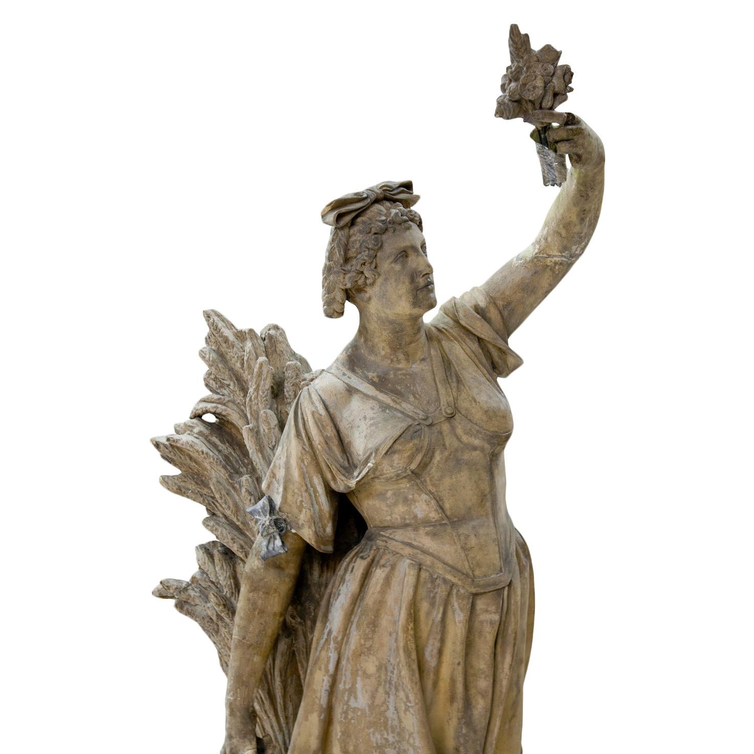 Life-sized terracotta sculpture of Ceres / Demeter, the Goddess of Harvest and Fertility. She holds a small boquet of flowers in her hand and stands in front of a large bundle of grains.